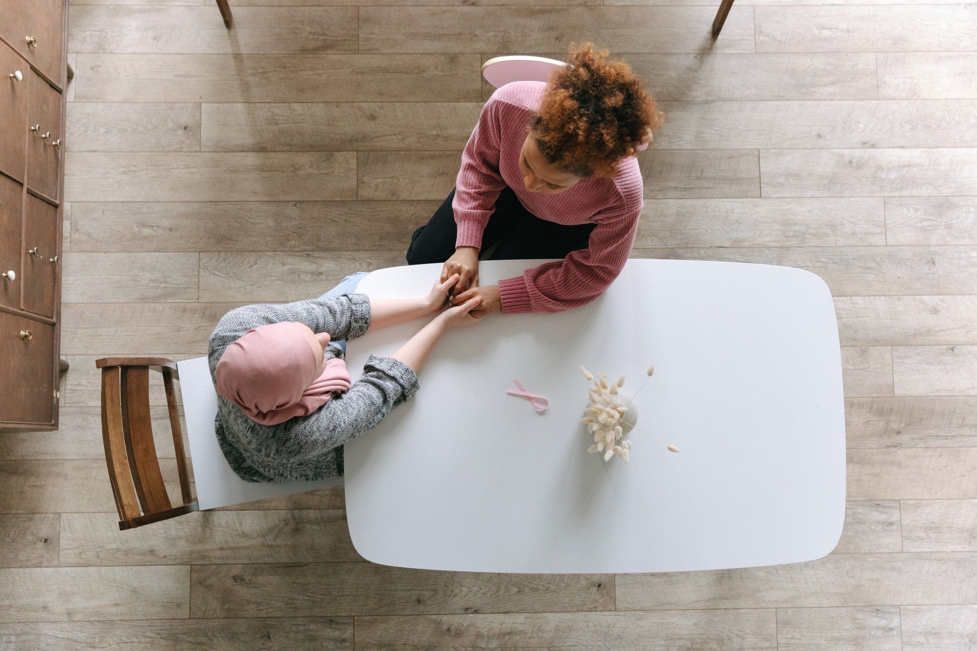 A woman holding the hand of a cancer patient while sitting at a table.