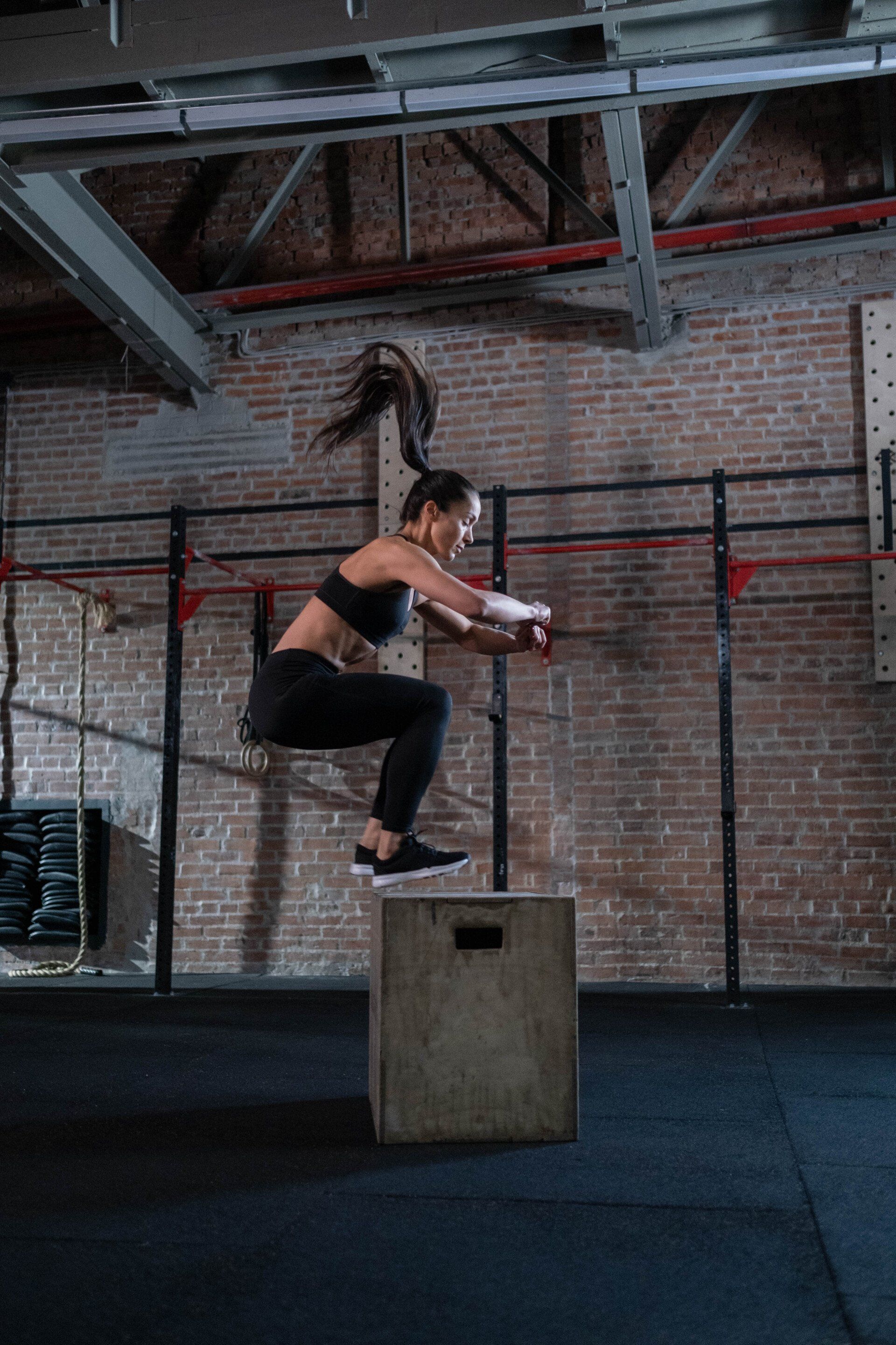 A woman is jumping on a box in a gym.