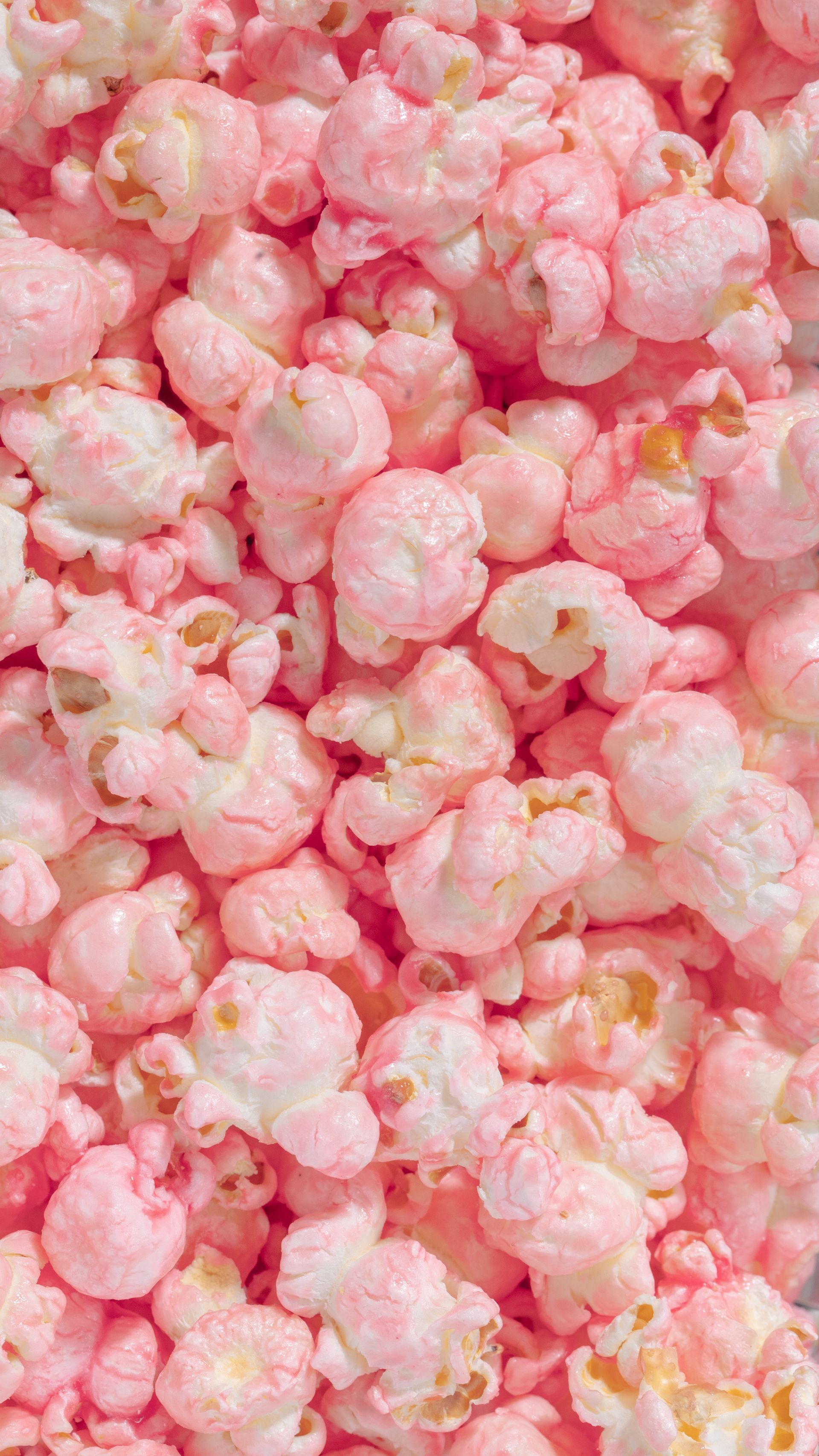 A close-up, top-down view of a large pile of light pink candy-coated popcorn.