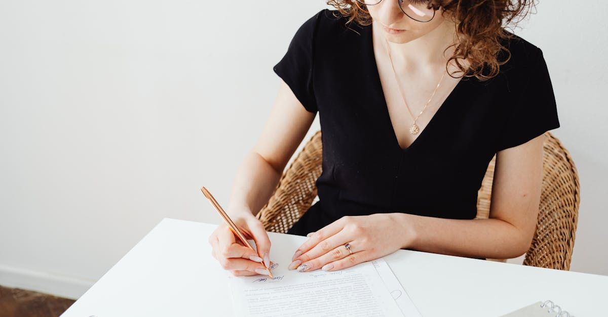 A woman is sitting at a table writing on a piece of paper with a pencil.