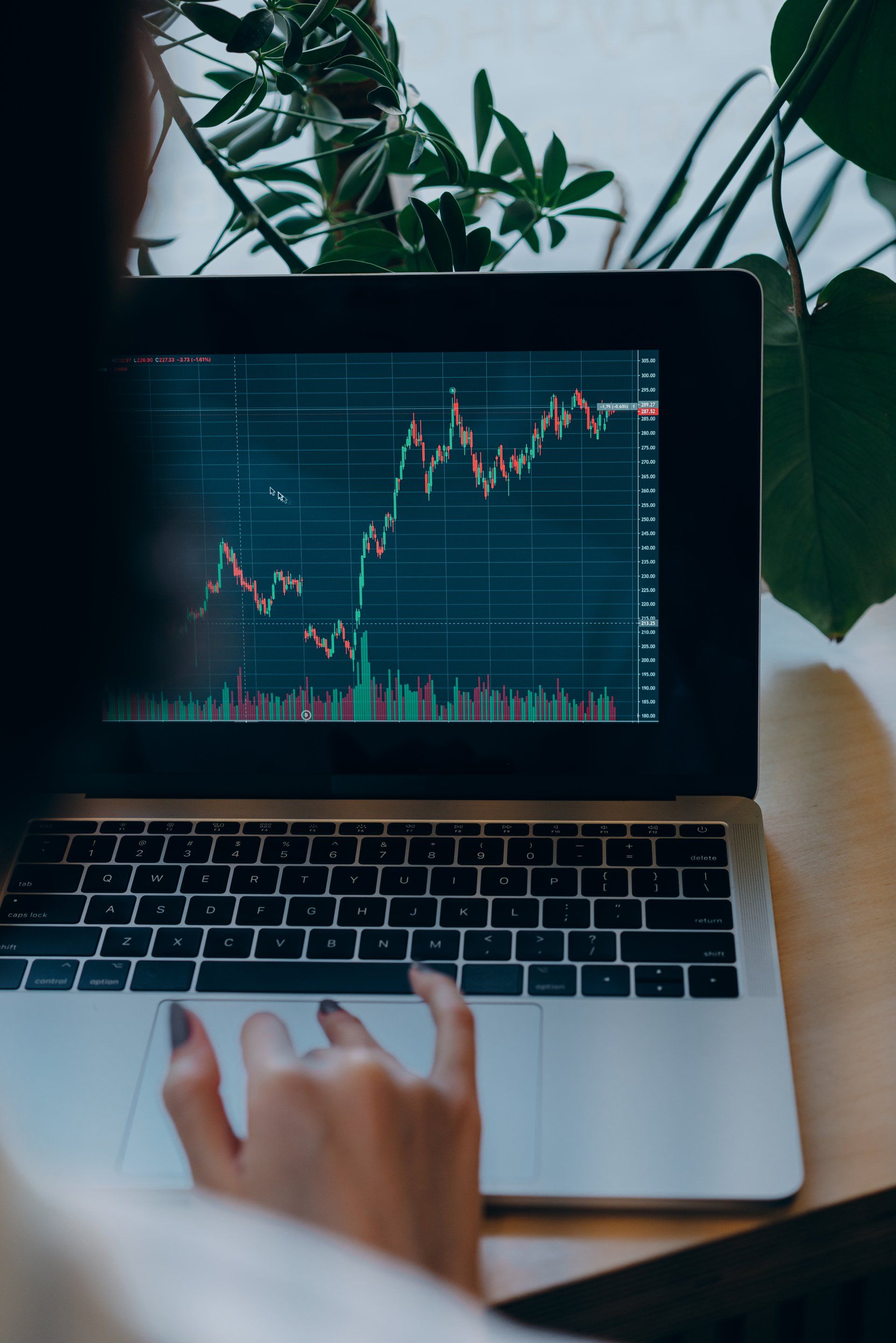 Person using a laptop, viewing a stock market graph with green and red lines.