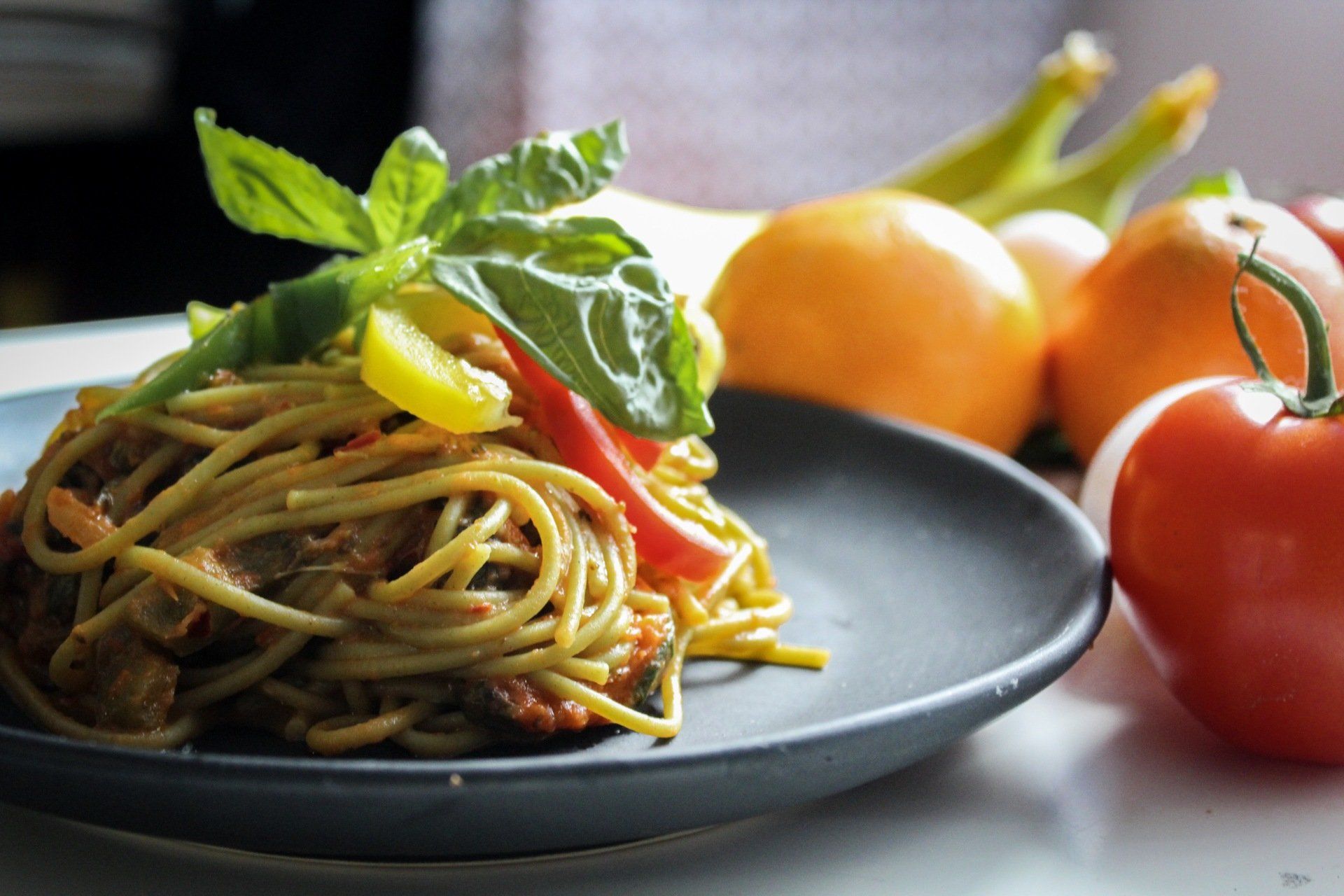 A black plate topped with spaghetti and vegetables