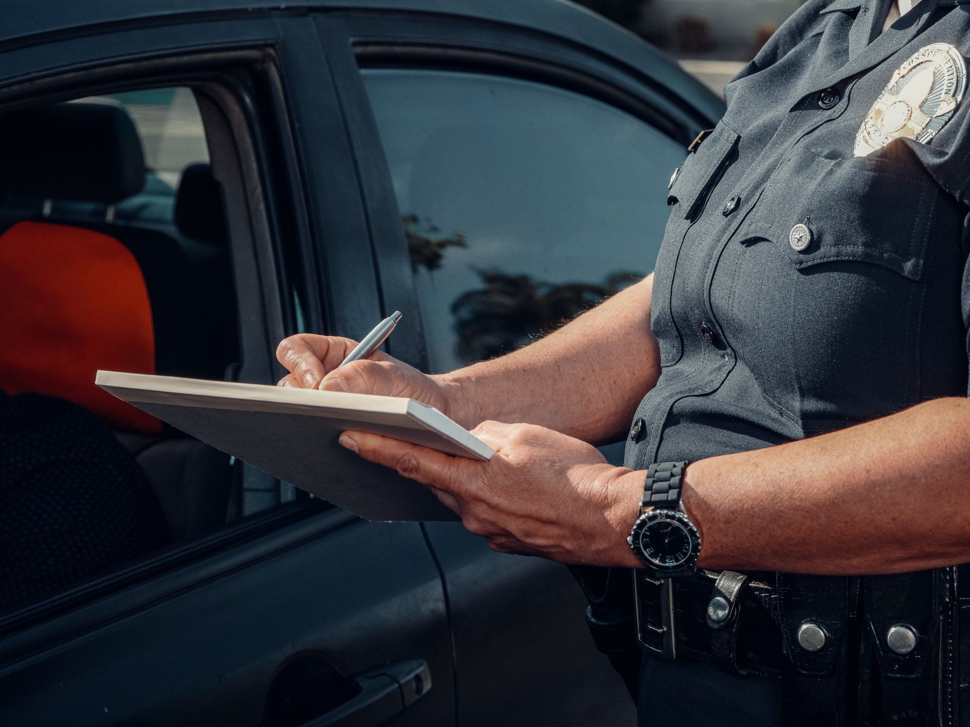 A police officer is writing on a clipboard in front of a car.