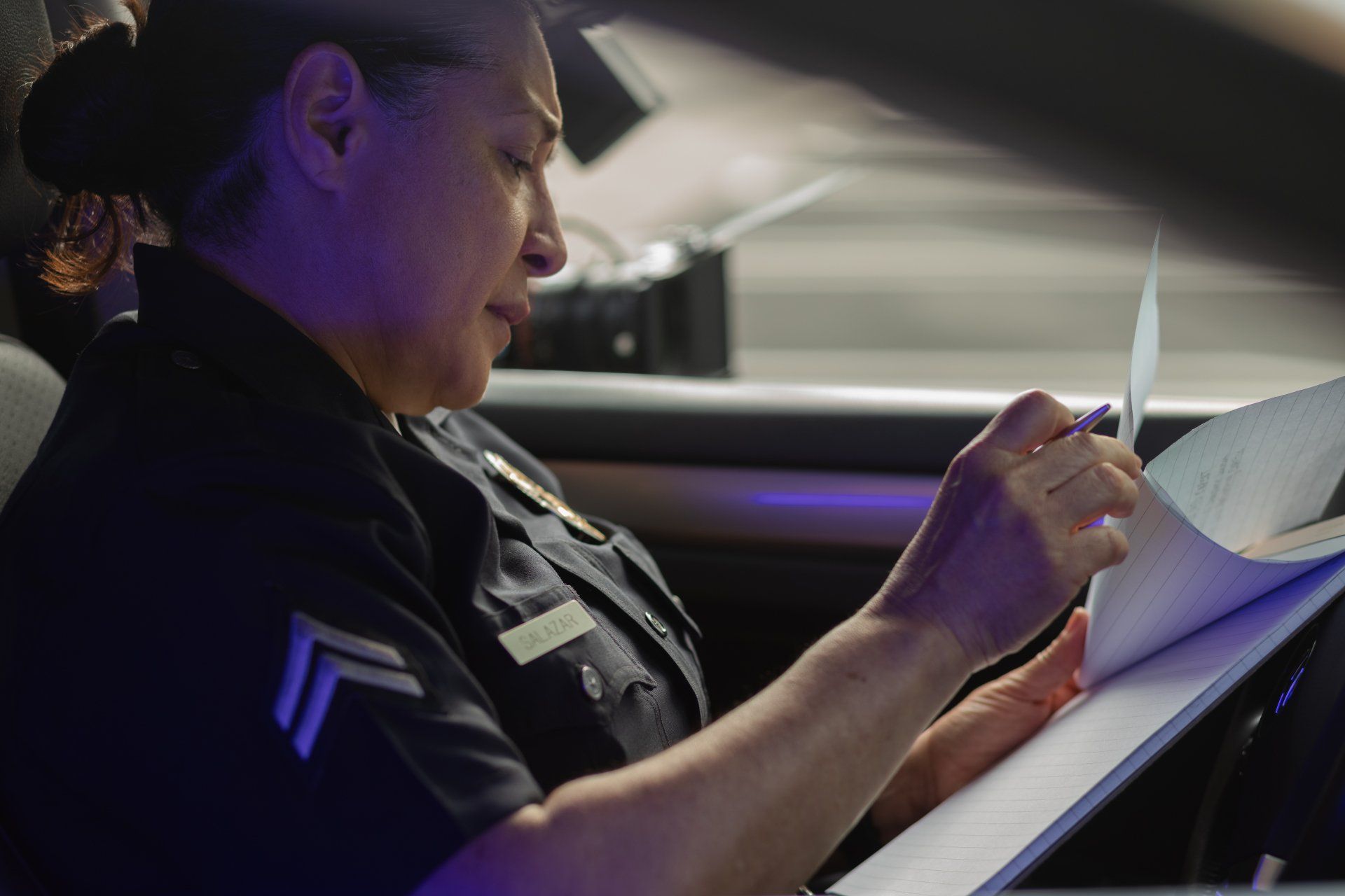 A police officer is sitting in a car reading a piece of paper.
