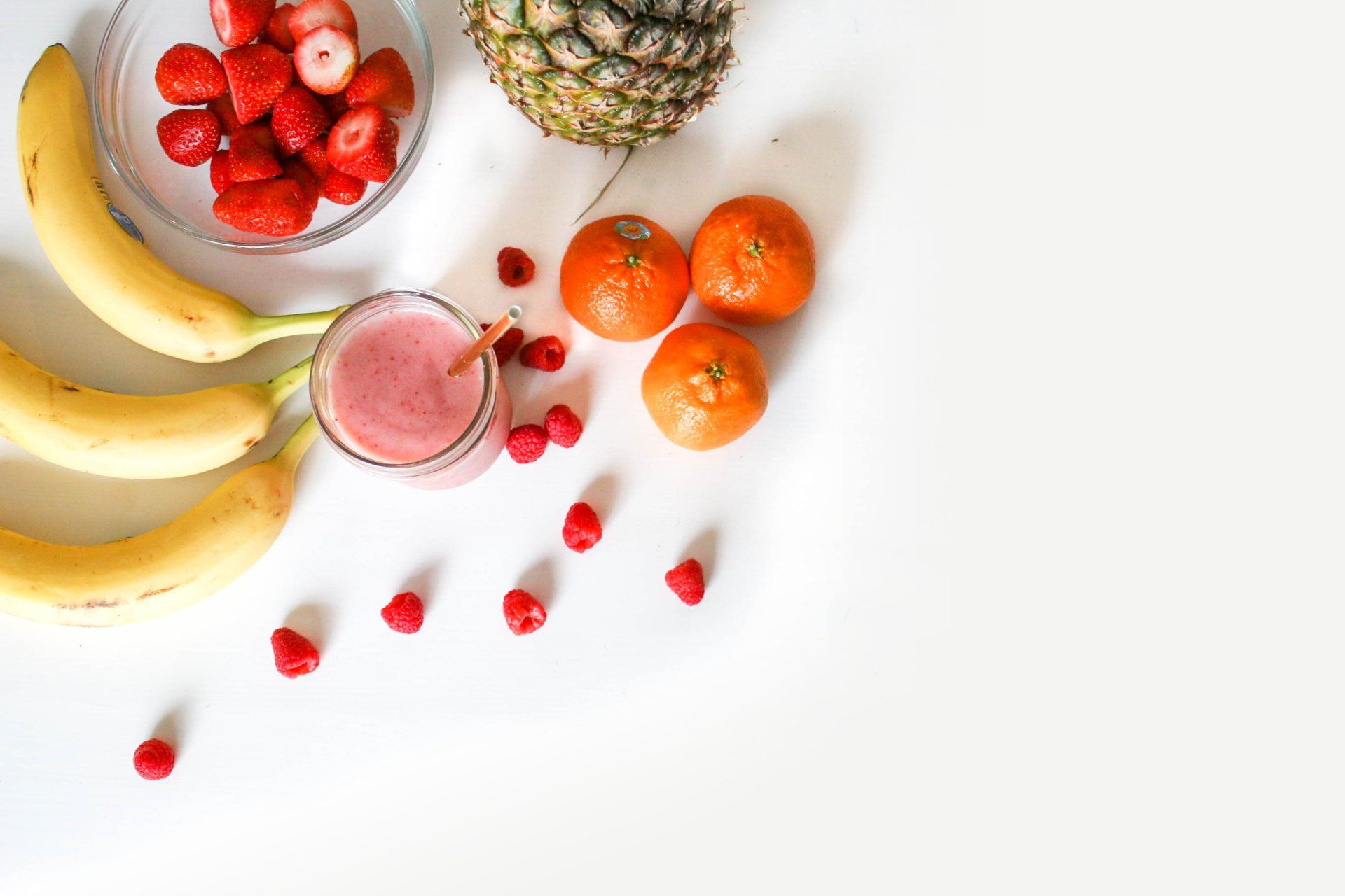 A variety of fruits and a smoothie on a white table.