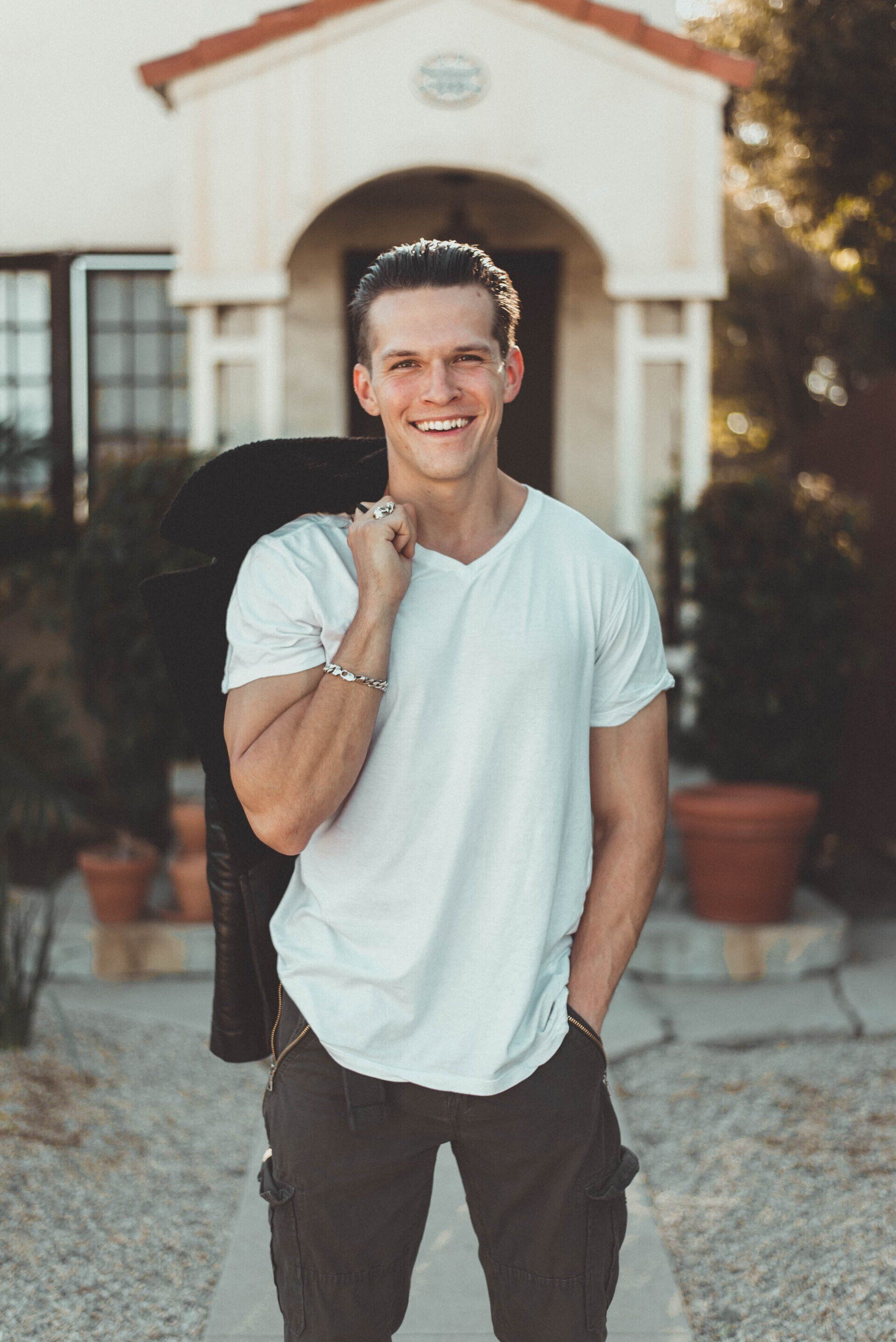 a man in a white t-shirt in front of a house holding a jacket over his shoulder is happy after his depression treatment