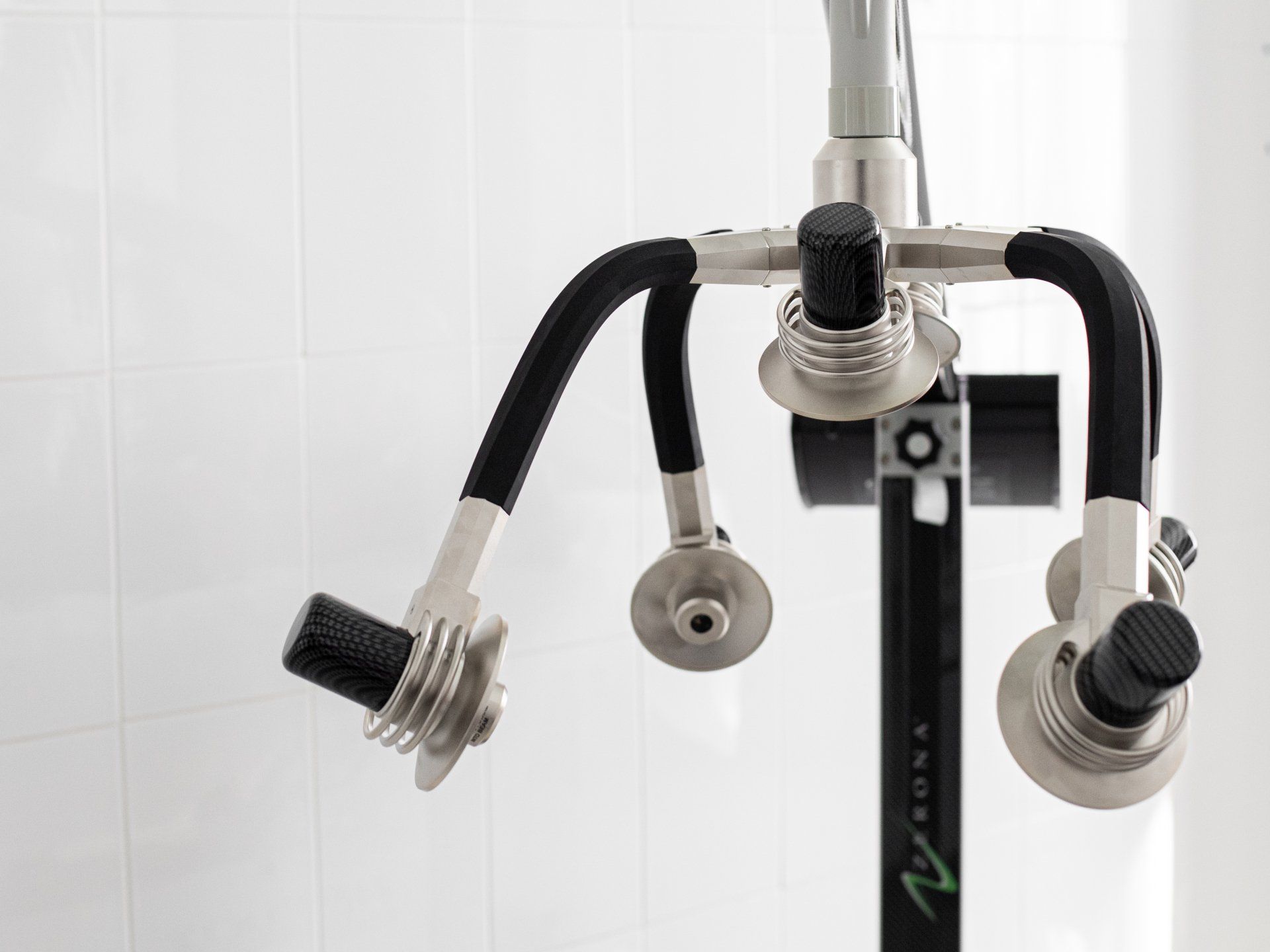 Medical robotic instrument with four black flexible arms against a white tiled background