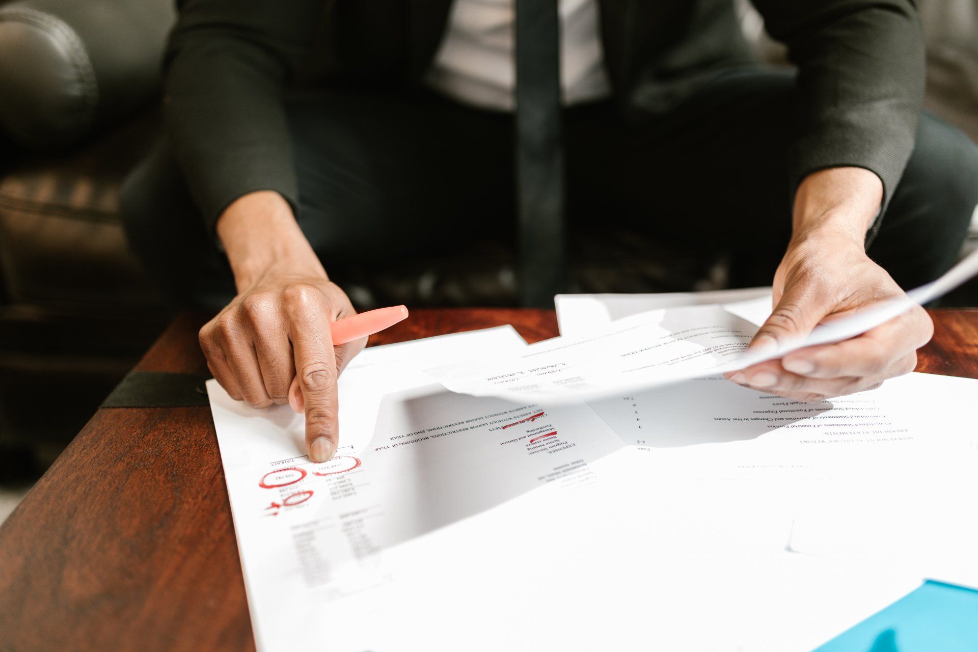 Person in a suit reviews documents, pointing at a paper with a red pen on a table.