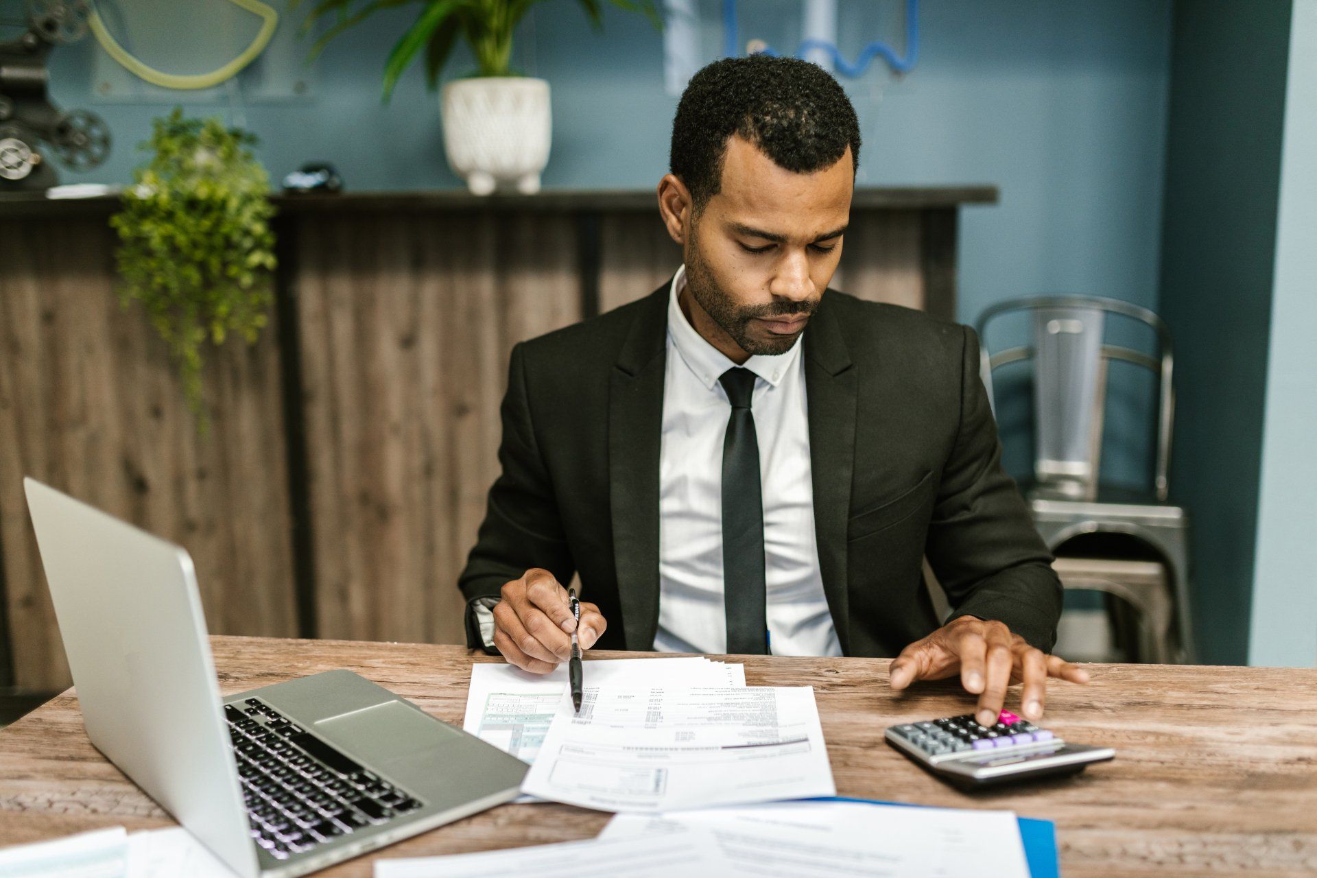 A man in a suit and tie is sitting at a desk with a laptop and a calculator.
