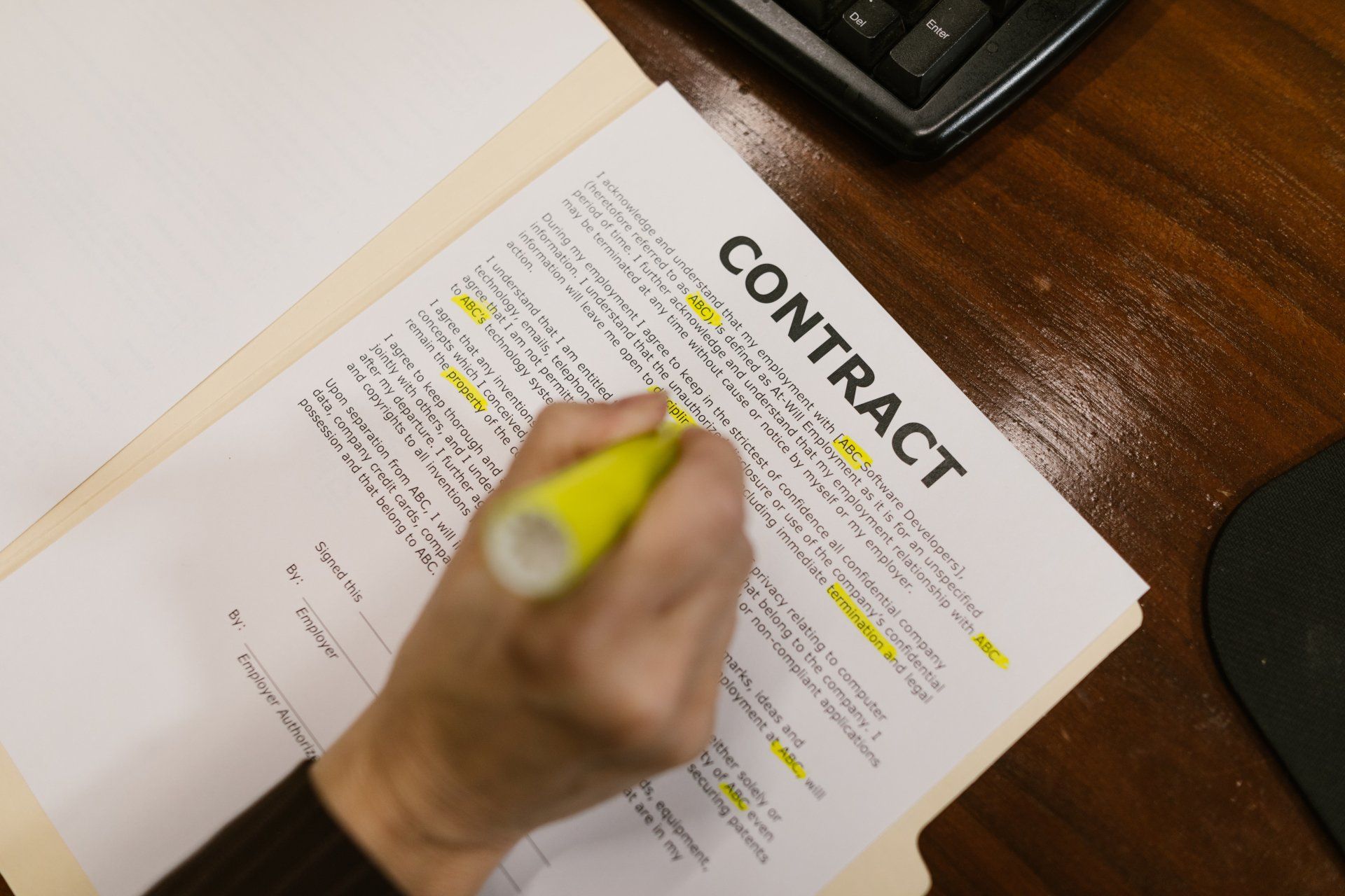 A hand uses a yellow highlighter to mark lines of text on a document titled CONTRACT.
