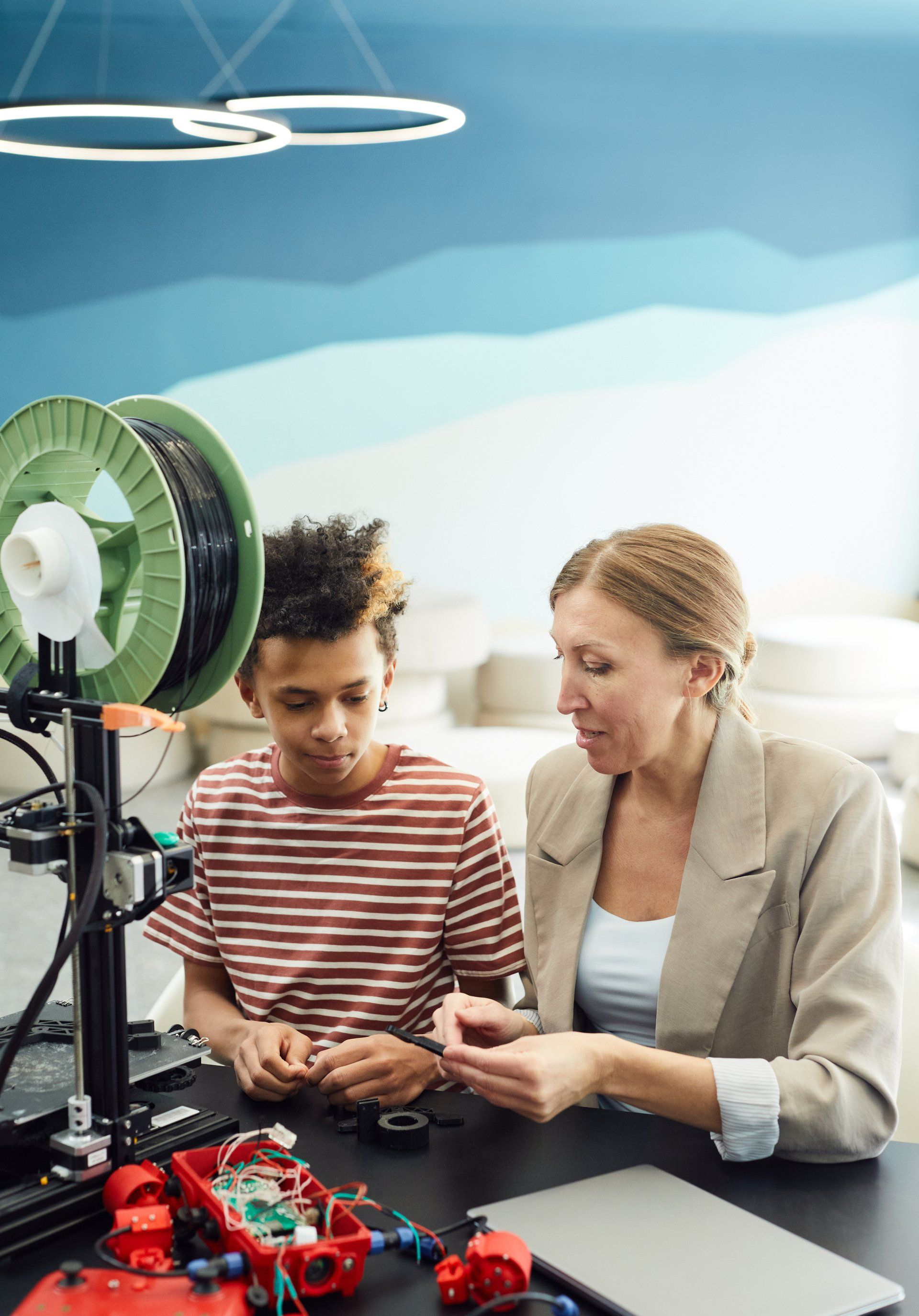 Woman and boy examine a 3D printer's components. Inside a classroom-like setting, they appear engaged with the machine.