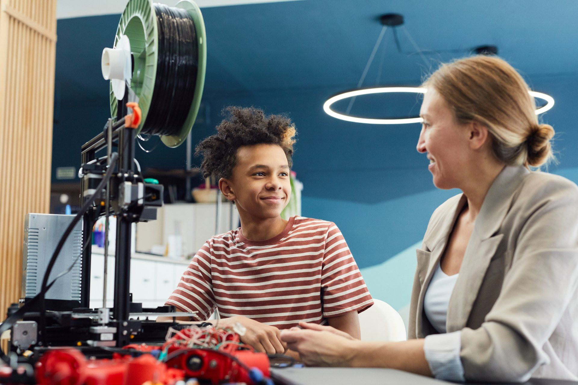 Eine Frau und ein Junge sitzen an einem Tisch vor einem 3D-Drucker.