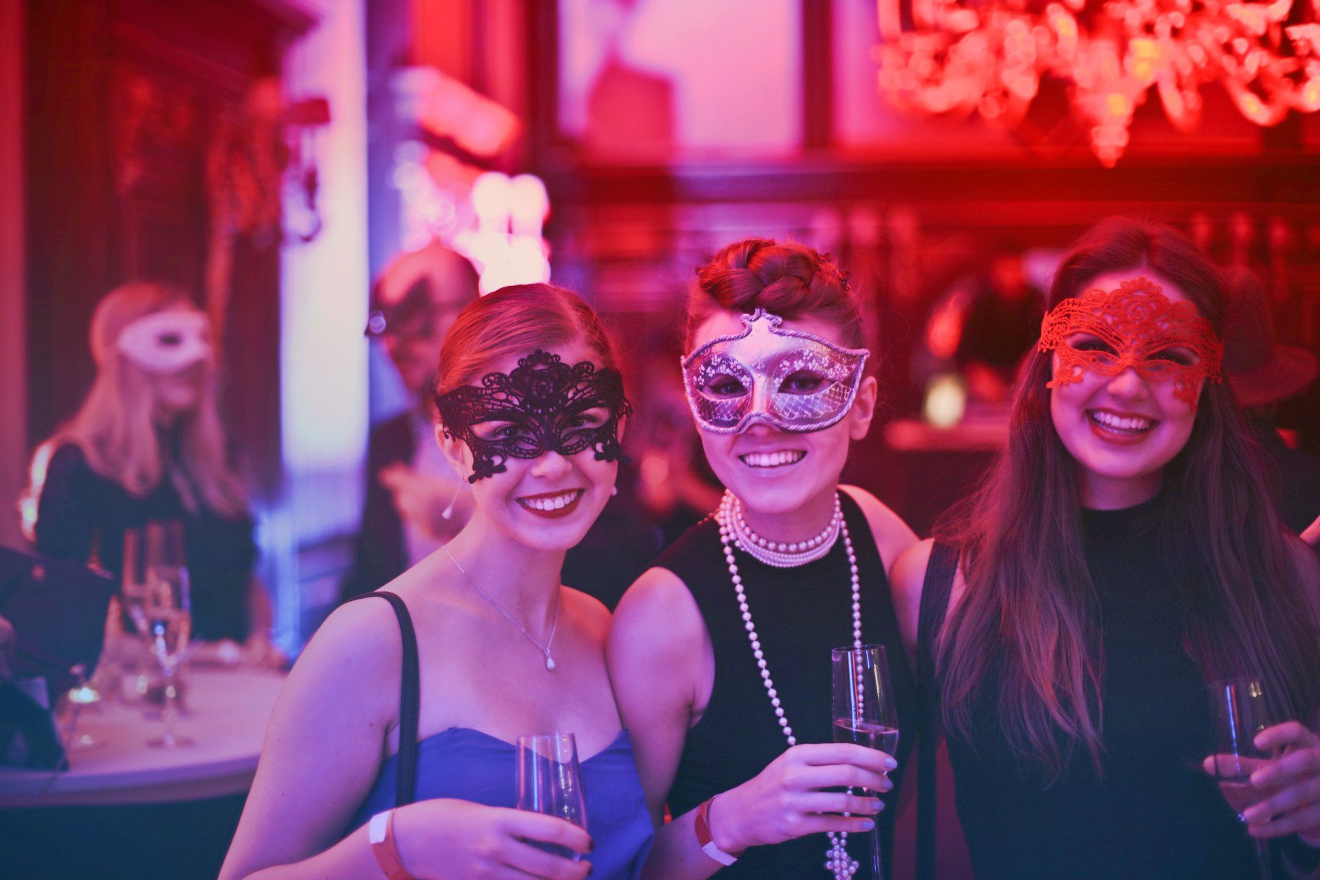 Three women wearing masks are posing for a picture at a party.