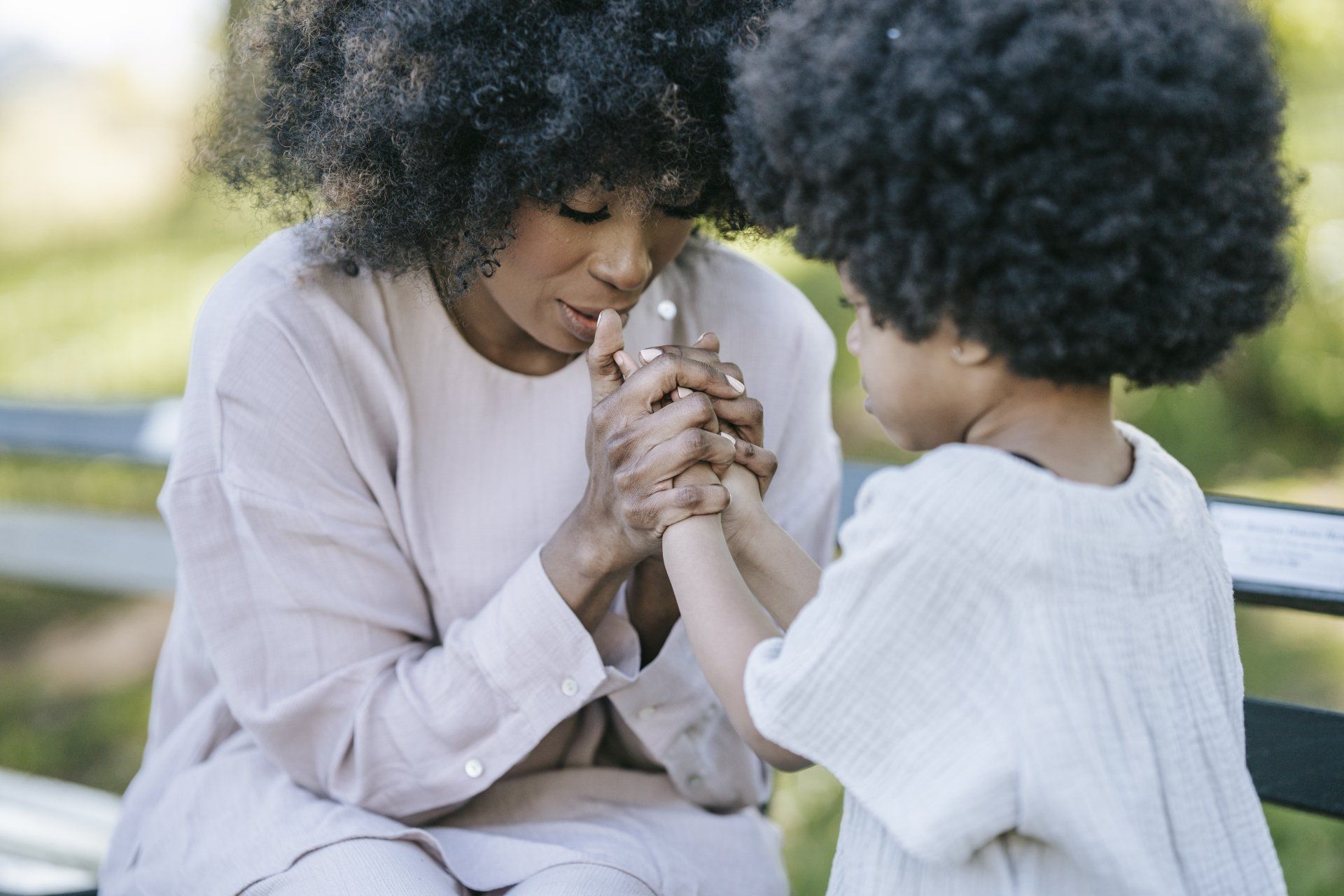 A woman and a child are sitting on a bench holding hands.