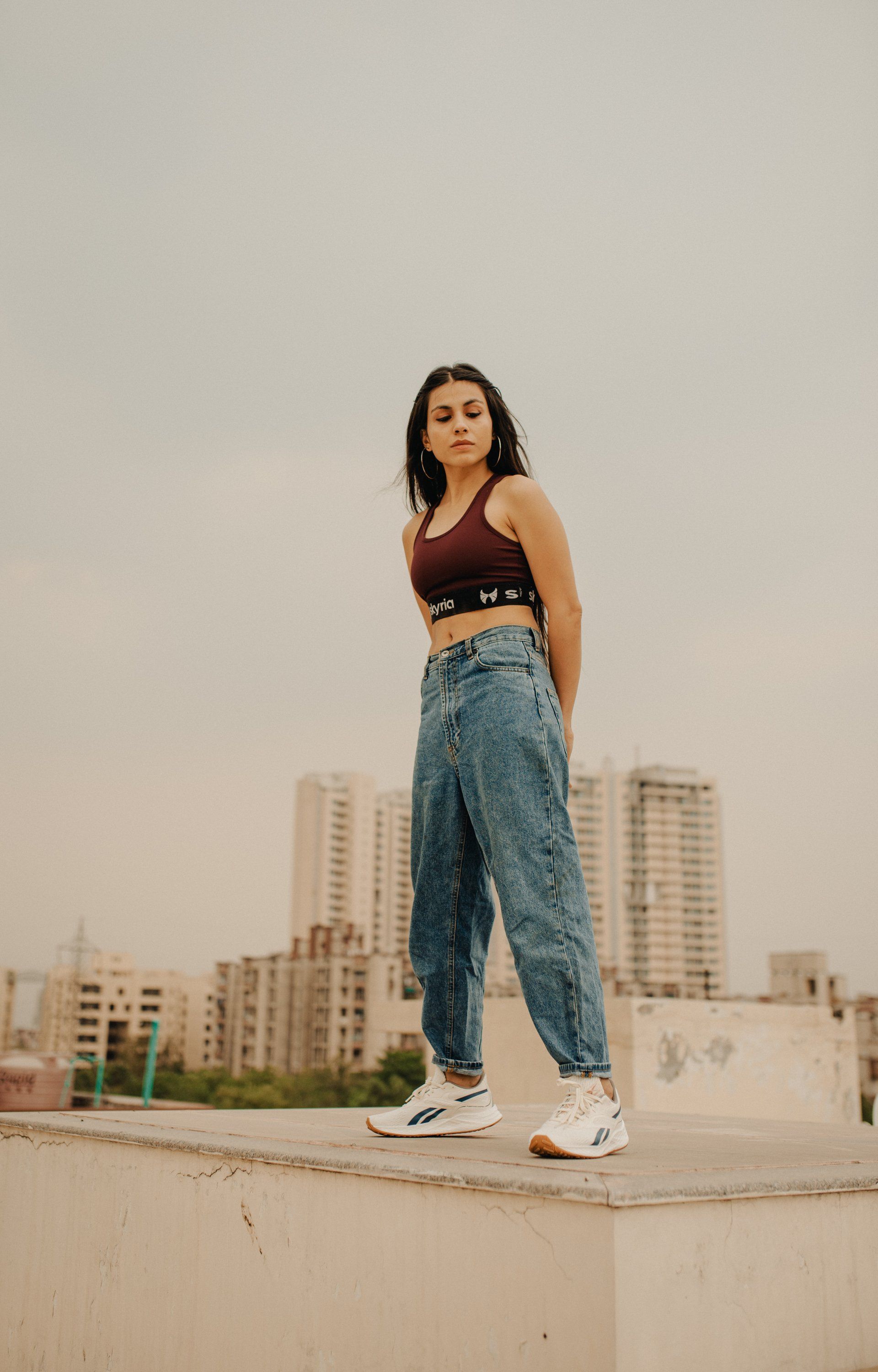 A woman in a crop top and jeans is standing on a ledge.