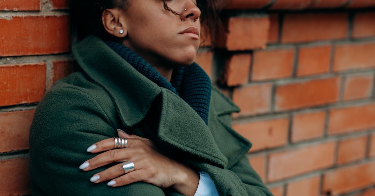 A woman in a green coat is leaning against a brick wall.