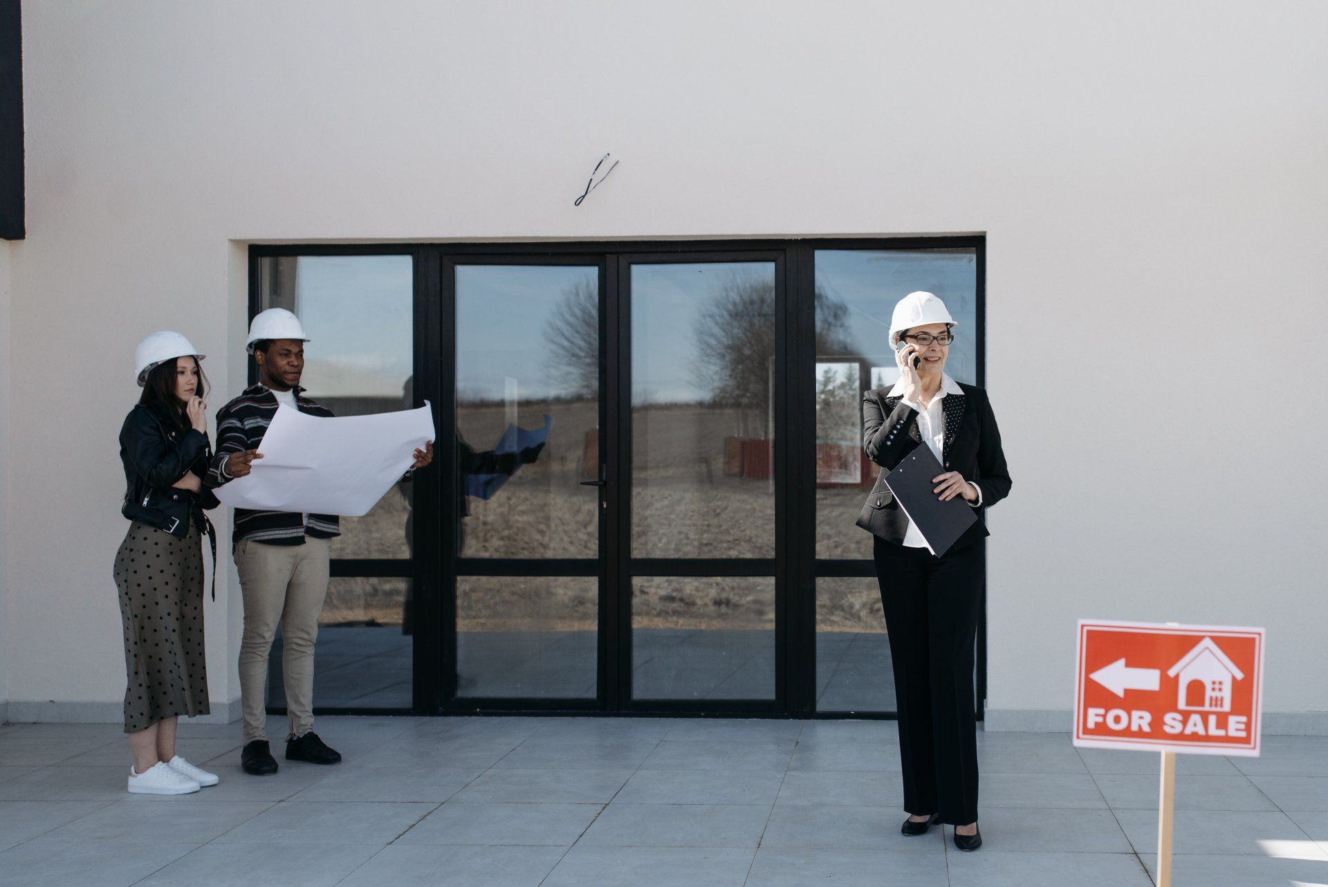 Three people in hard hats looking at a blueprint in front of a house with a 