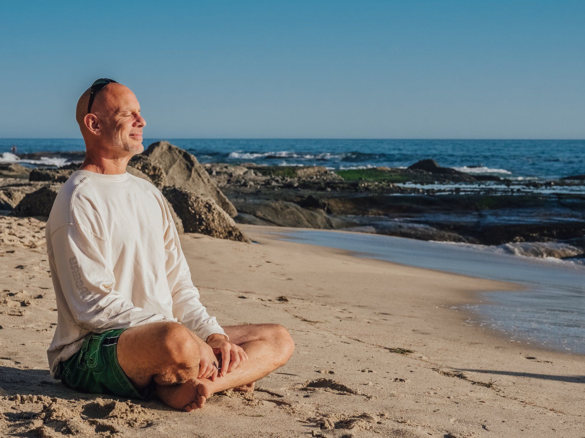 A man is sitting in a lotus position on the beach.
