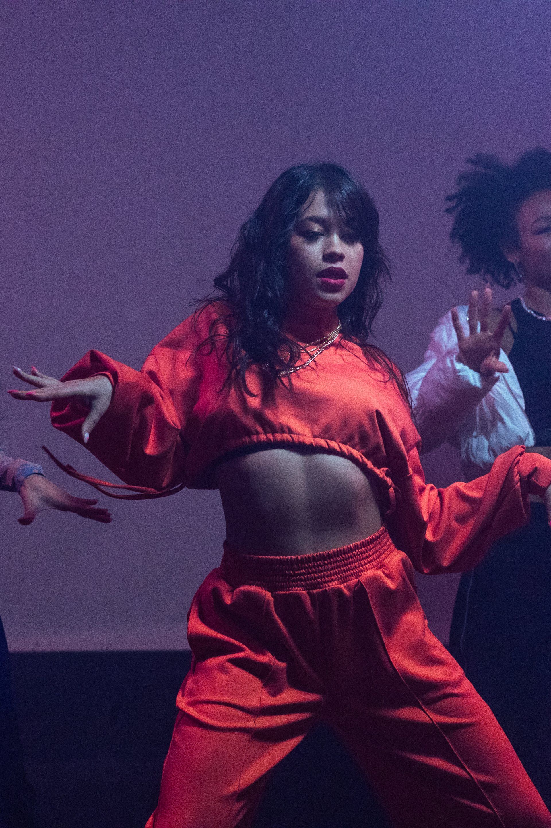 a woman in a red crop top and red pants is dancing on a stage .