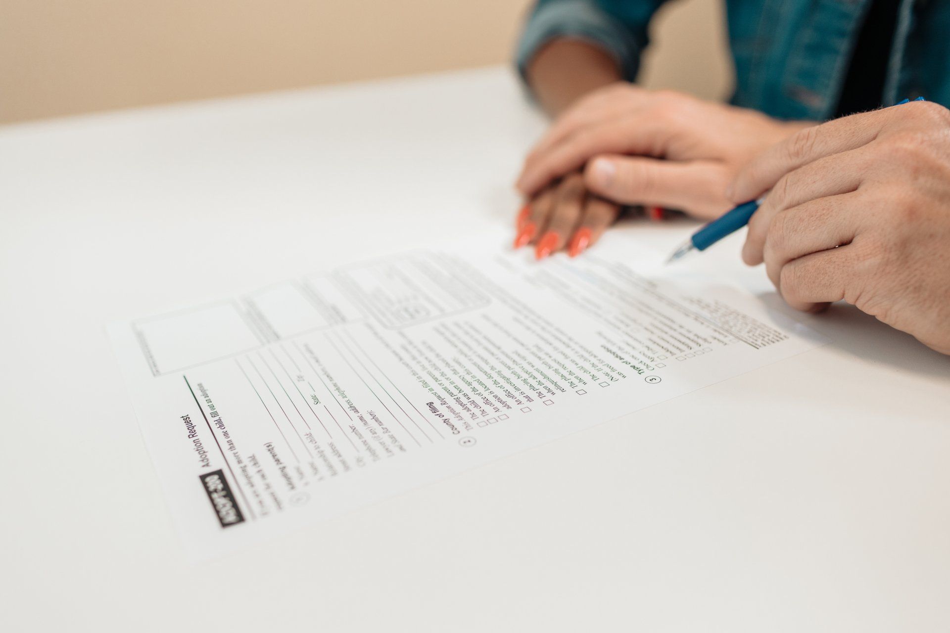 Hands over a document on a white table; one hand holds a pen, another rests gently on the other person's hand.