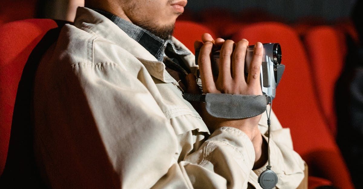 A man is sitting in a theater holding a camera in his hands.