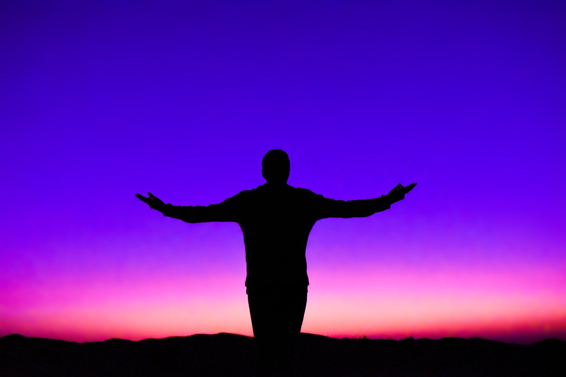 A silhouette of a man with his arms outstretched at sunset.