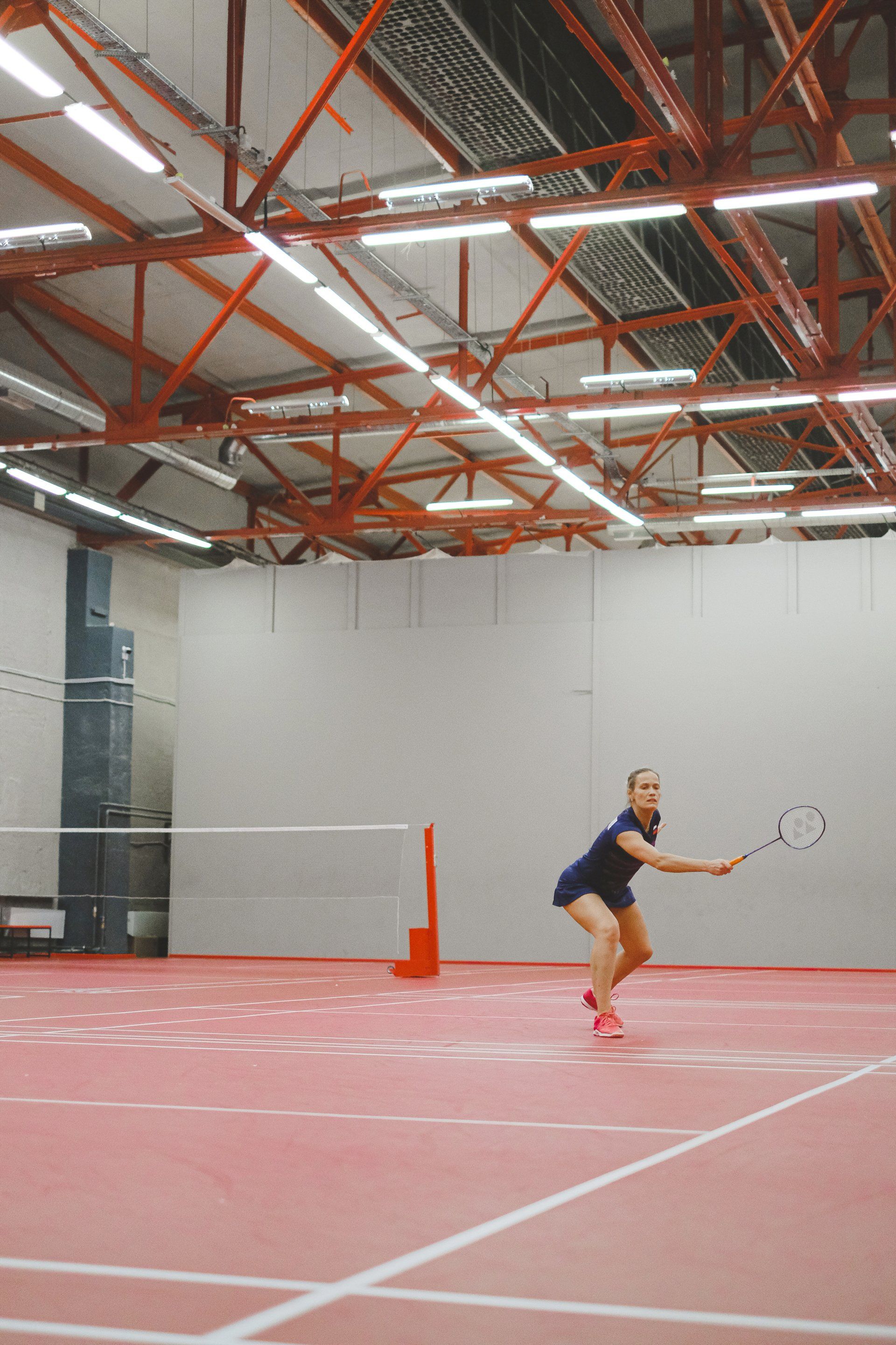 A woman is playing tennis on a red court in a gym.