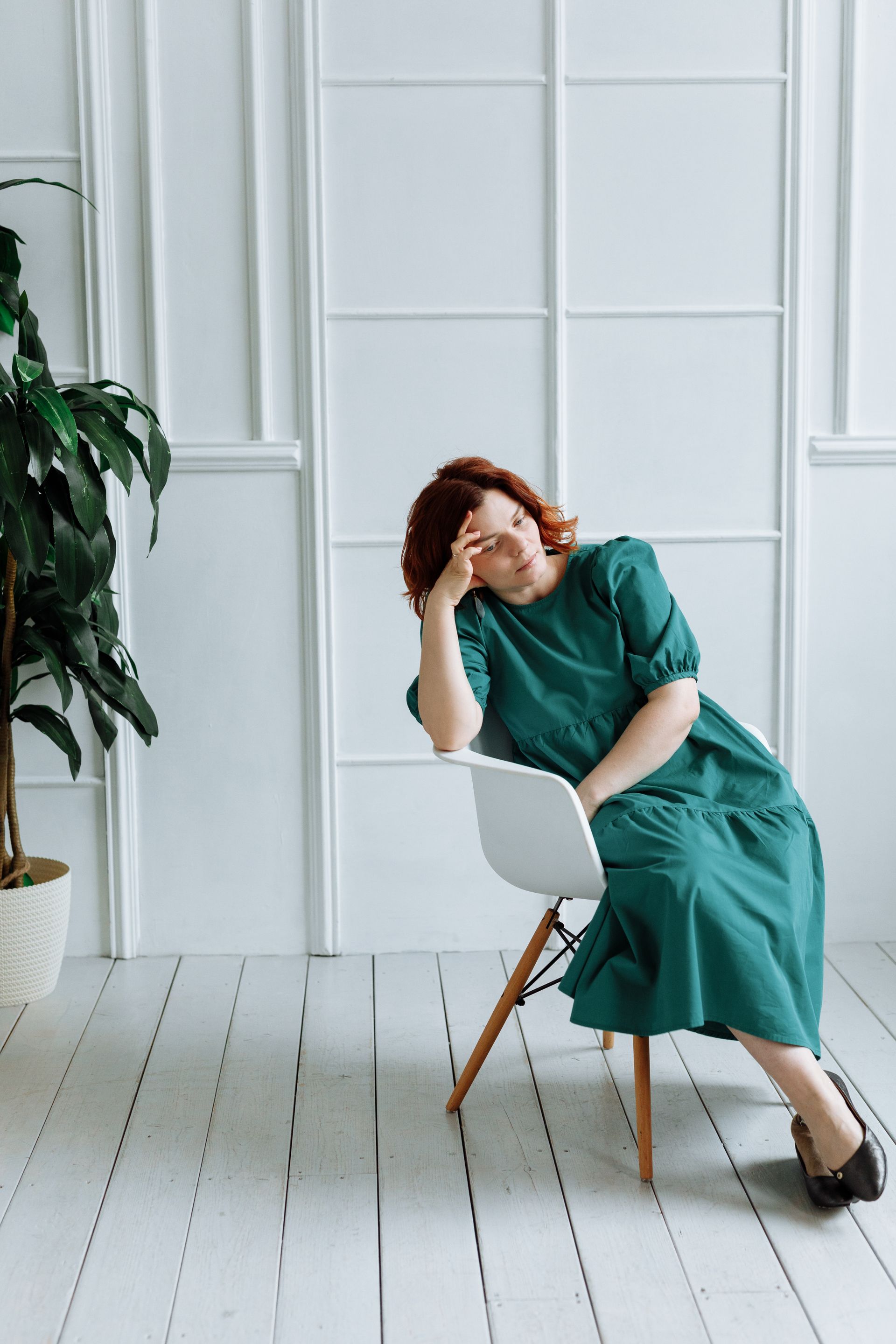 Une femme en robe verte est assise sur une chaise blanche.
