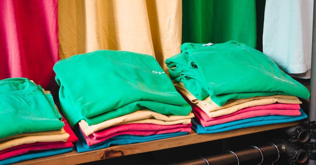 Stapels opgevouwen T-shirts in verschillende kleuren: groen, roze, geel, blauw en rood.