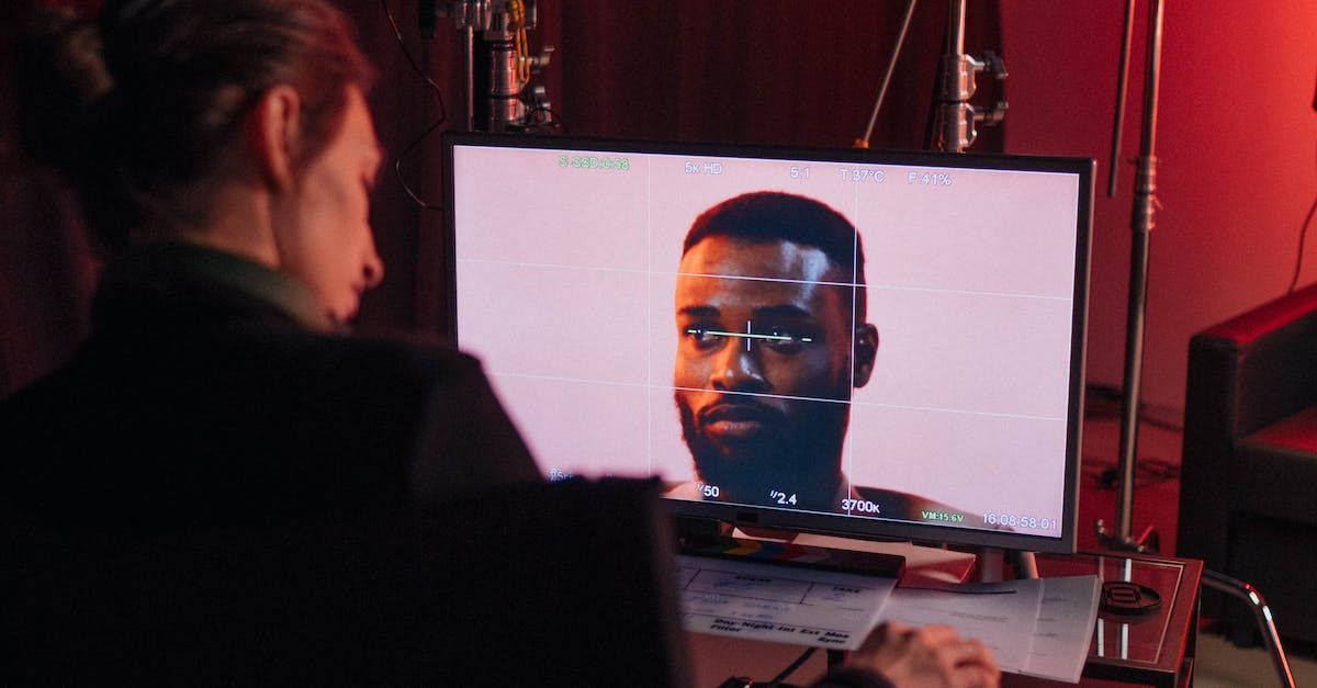 A woman is looking at a man 's face on a computer screen.
