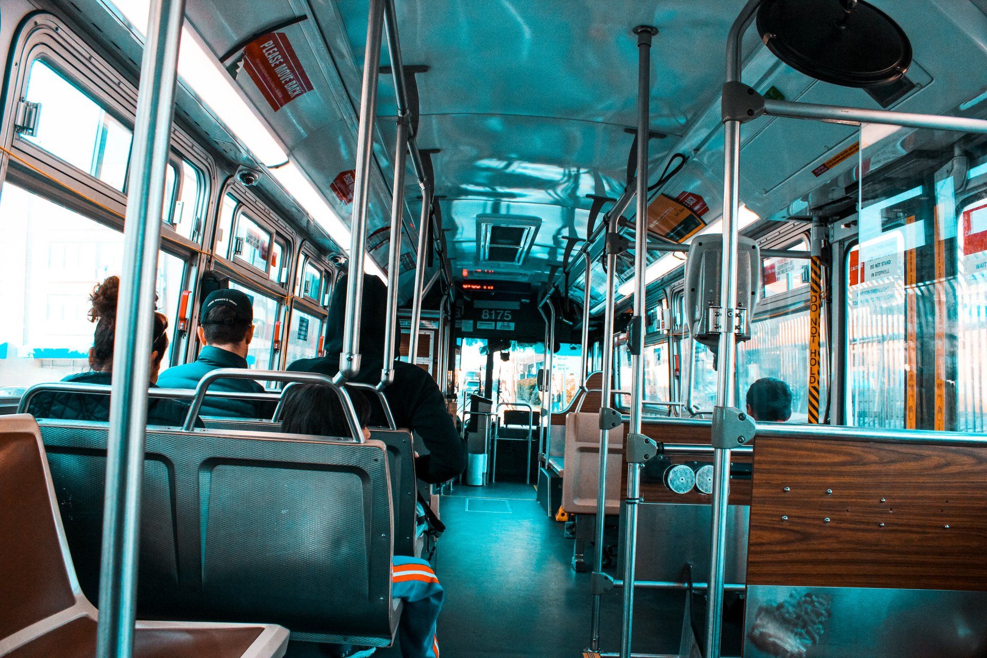 Interior of a city bus; people seated, metal poles, windows. Mostly blue and brown tones.