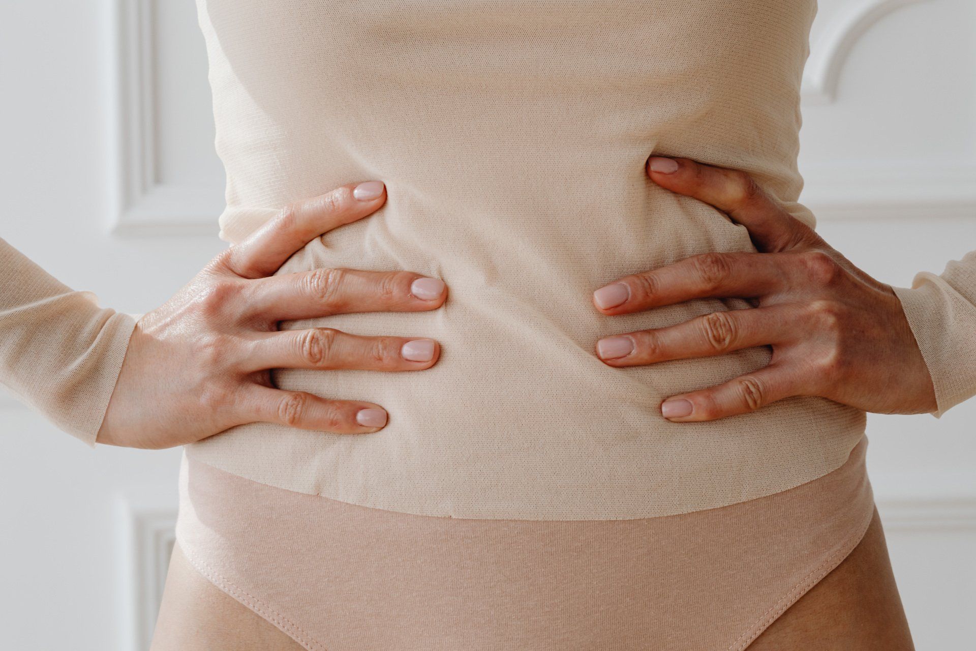 Hands gently holding a pregnant belly in a light beige outfit