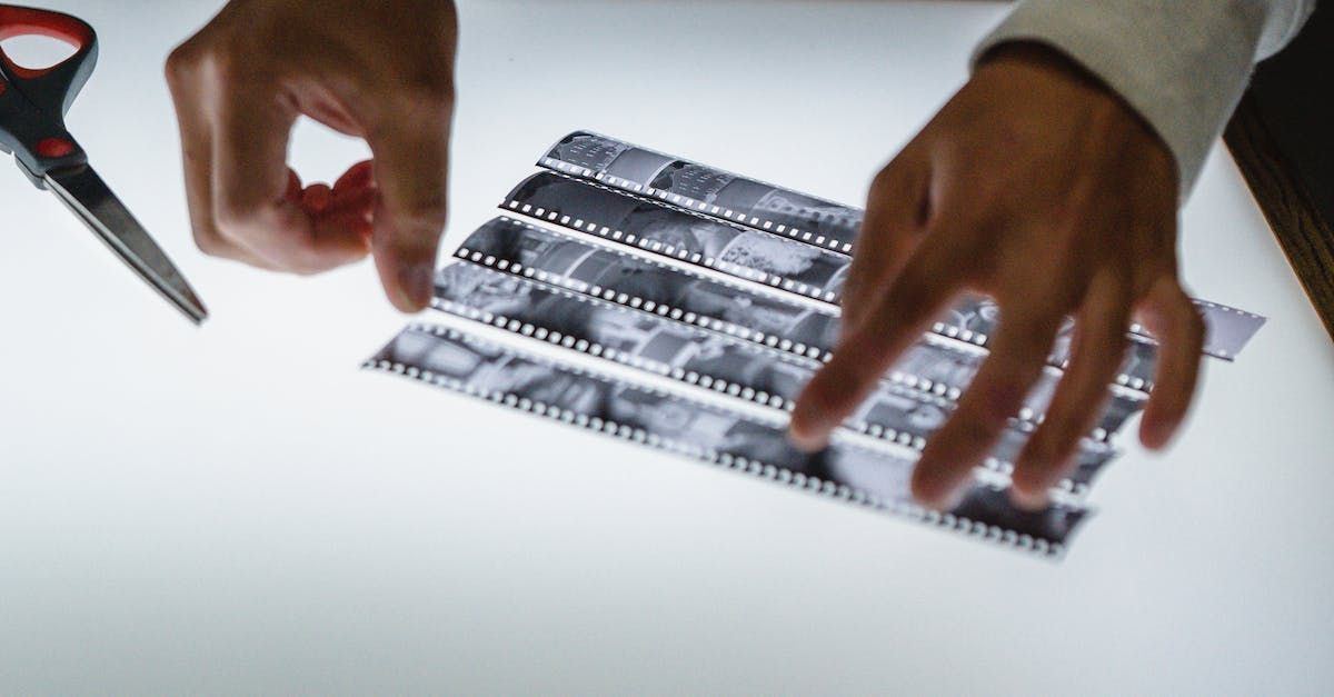Hands cutting a strip of film negatives with scissors on a light table