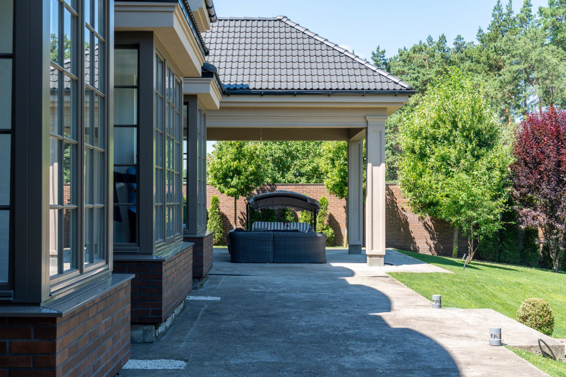 Exterior of a house with covered patio and a large seating area, surrounded by trees and lawn.