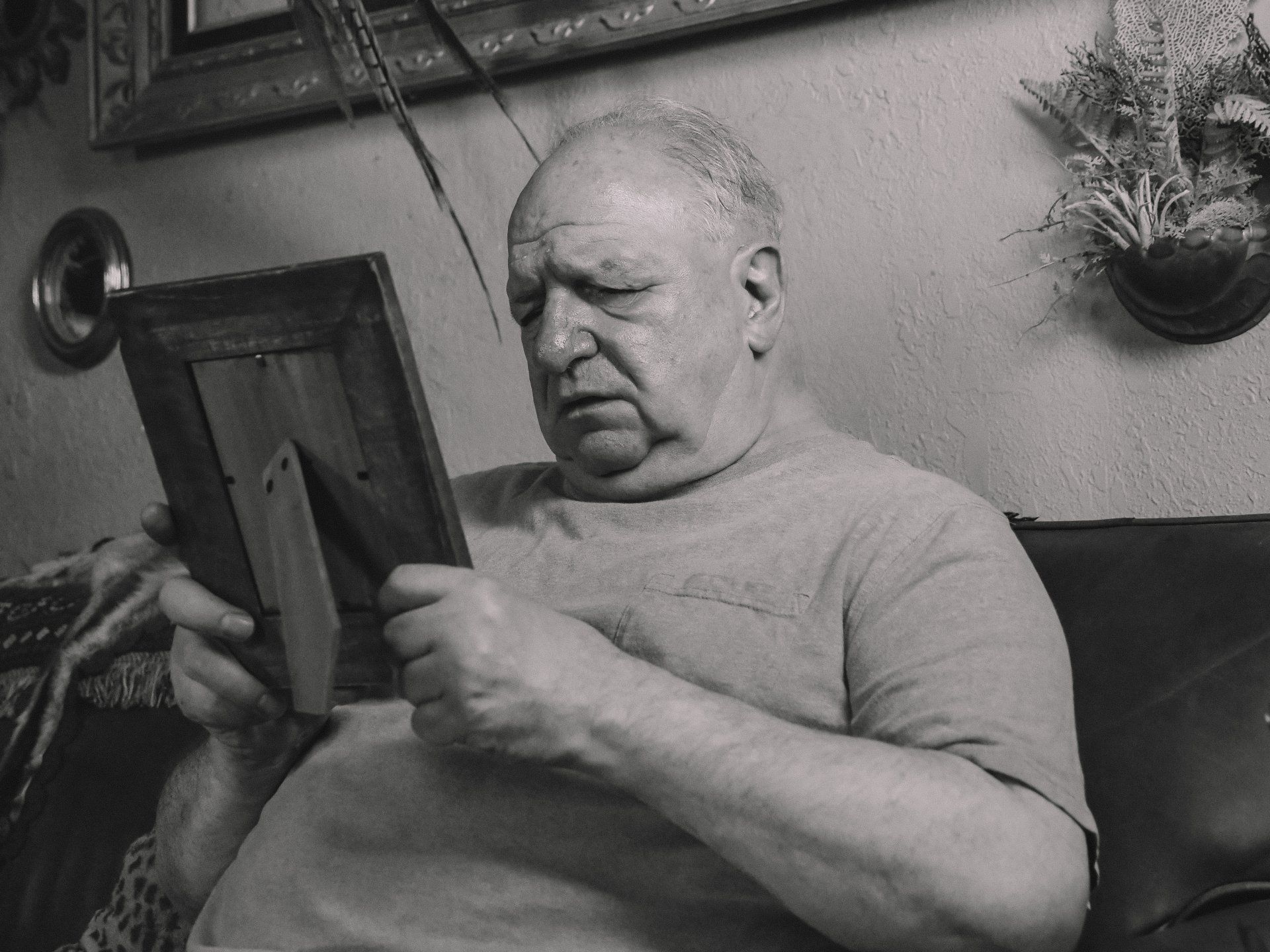 an elderly man is sitting on a couch looking at a picture frame .