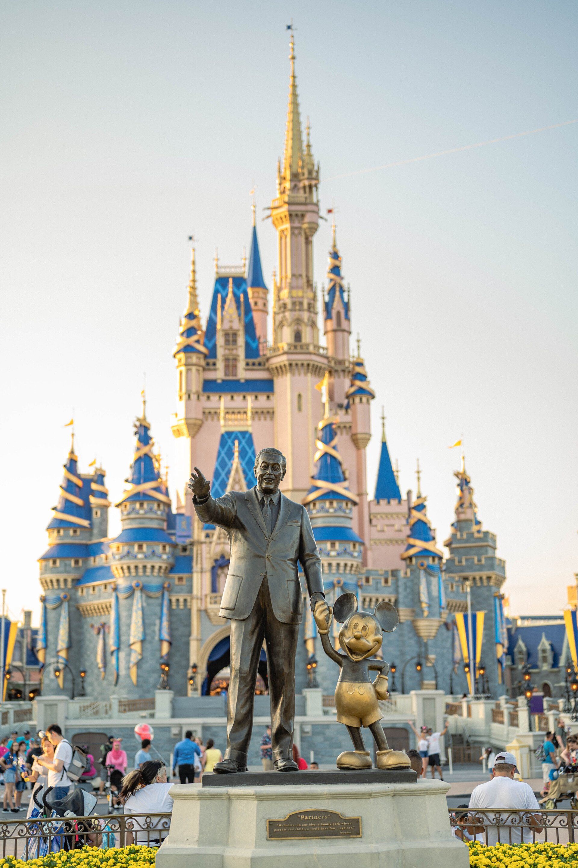 A statue of walt disney and mickey mouse in front of a castle.