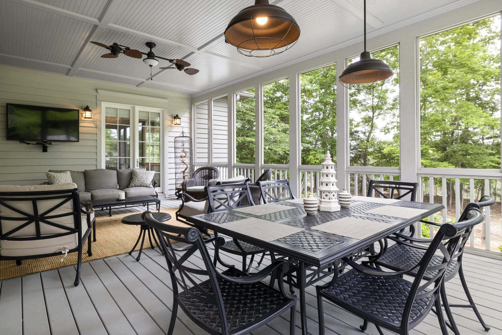 Screened-in porch with outdoor dining set and lounge area; gray and black tones, view of trees.