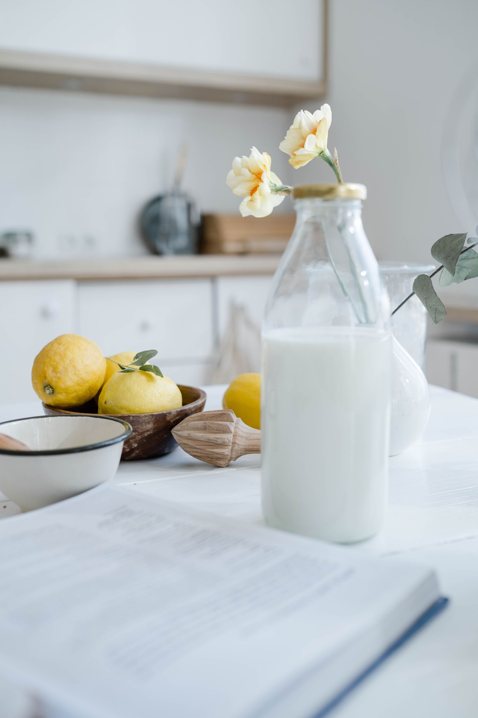 A bottle of milk is sitting on a table next to a bowl of lemons.