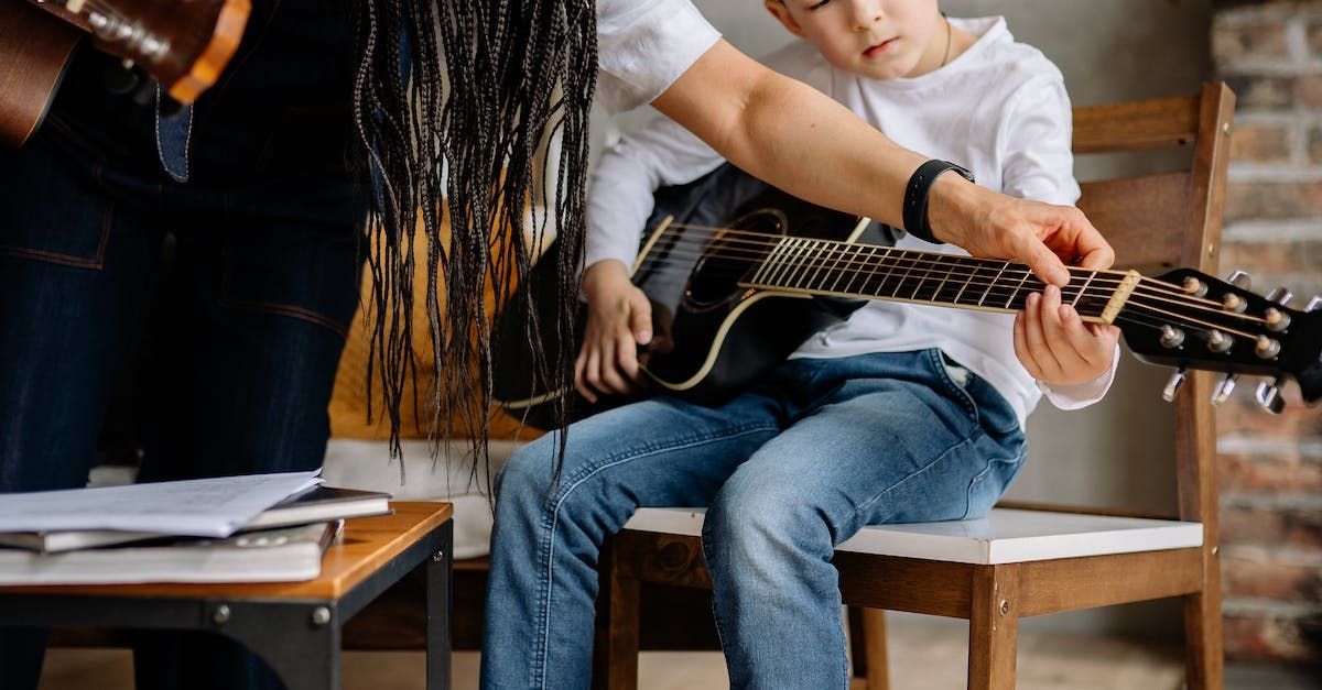 A man is teaching a young boy how to play a guitar.