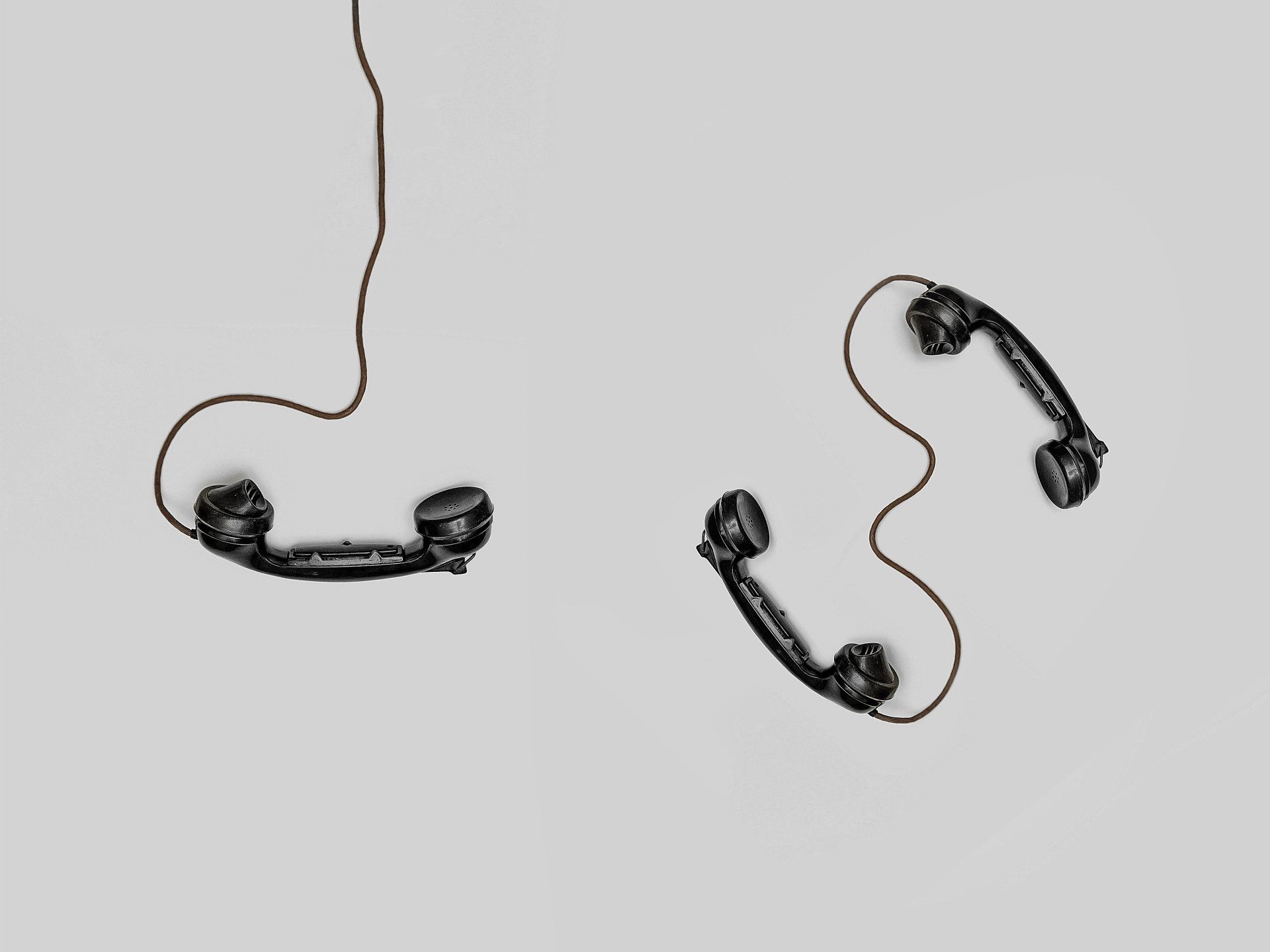 Three old fashioned telephones hanging from a cord on a white background.