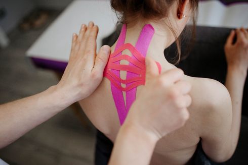 A woman is getting kinesio tape applied on her back to restrict painful movement and increase blood flow in Littleton, CO.