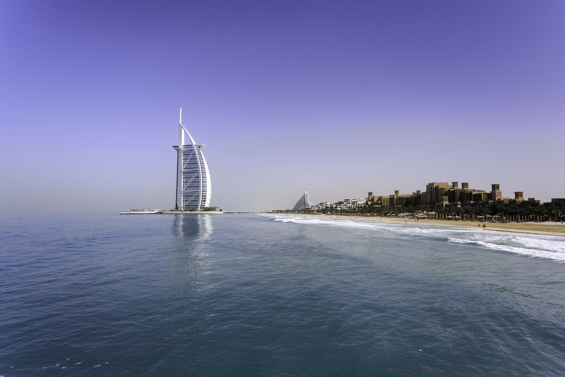 A large building is sitting on top of a body of water next to a beach.
