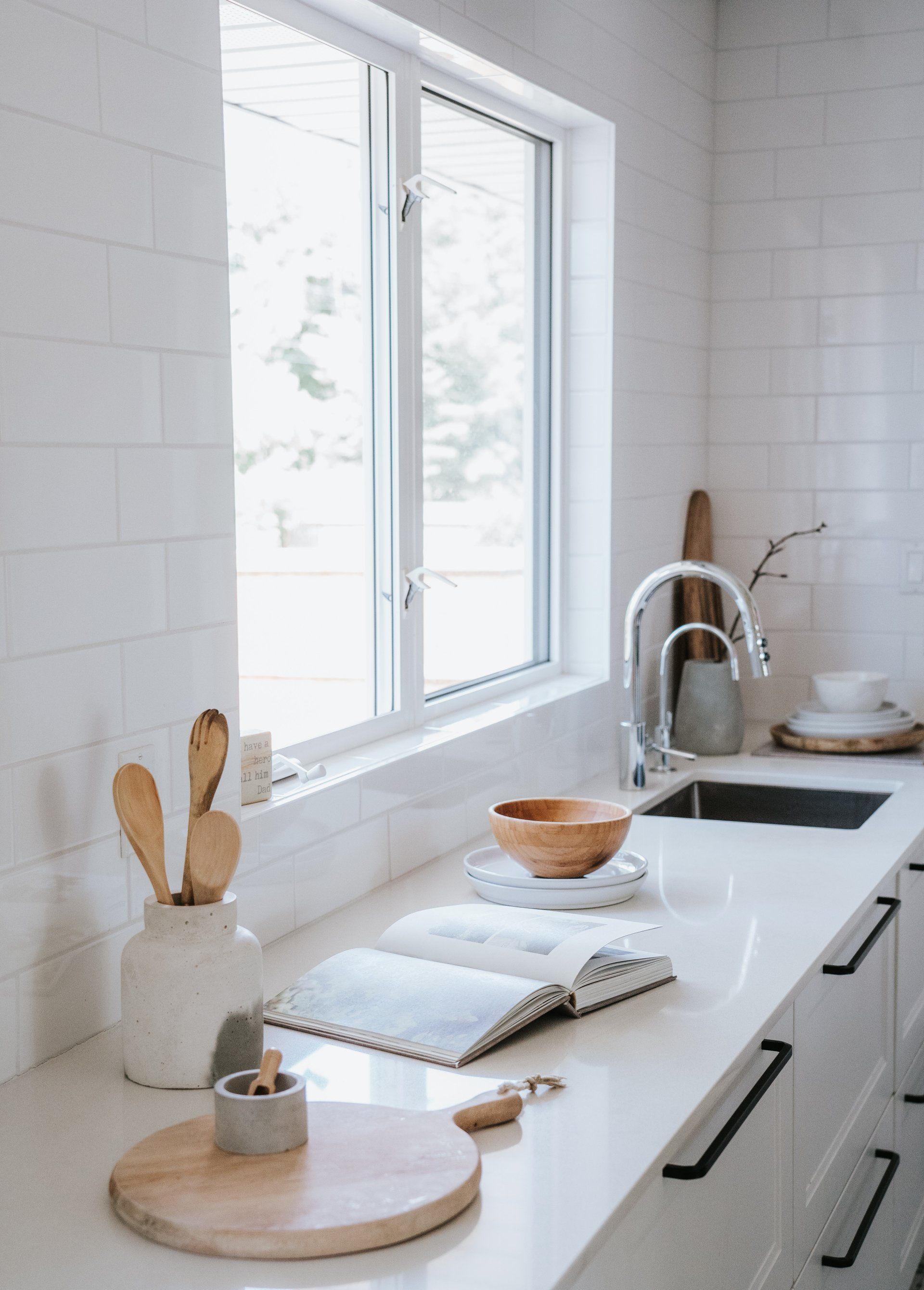 A kitchen with white cabinets , a sink , a window and a book on the counter.