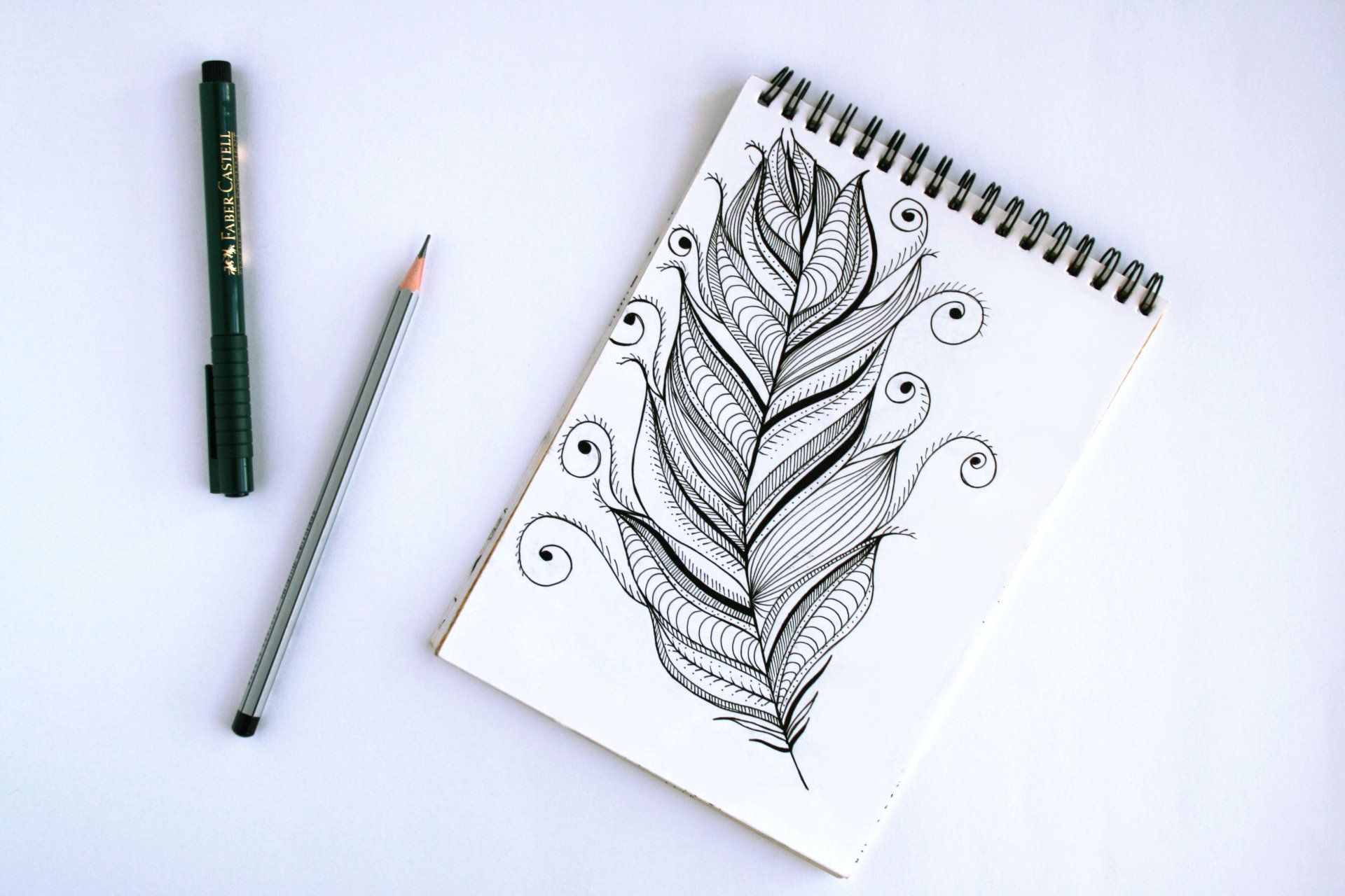 Un dessin d'une plume sur un cahier à côté d'un stylo et d'un crayon
