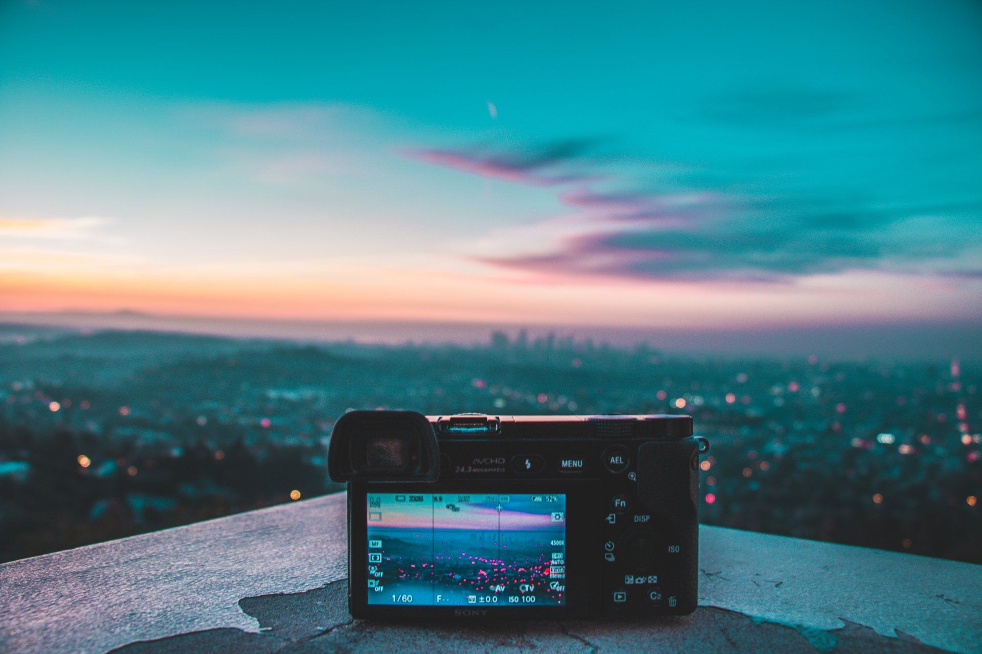 A camera is sitting on a ledge overlooking a city at sunset.