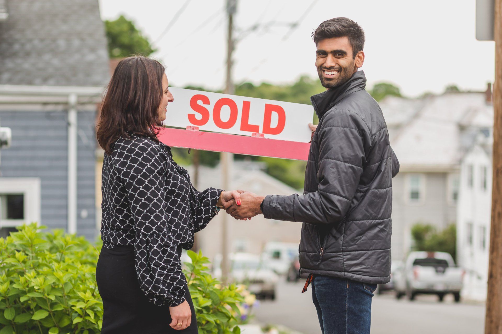 Woman and man shaking hands in front of a house, holding a 