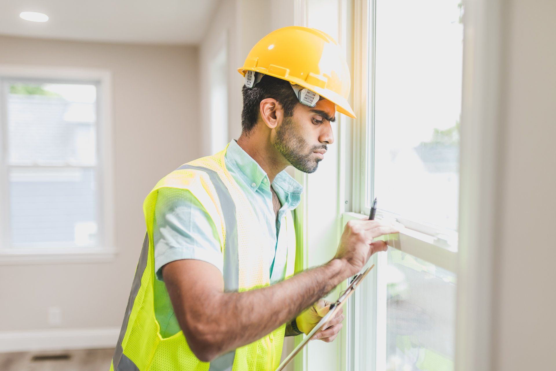 Worker in a yellow hard hat painting a window frame in a bright room