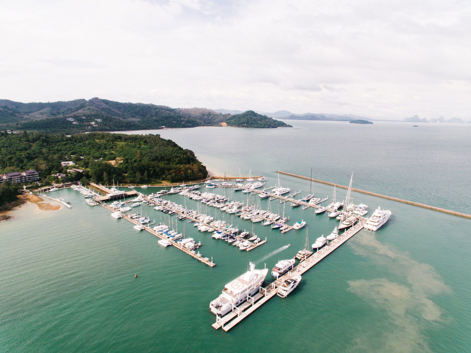 Aerial view of a marina with many white boats beside a green shoreline and calm blue water