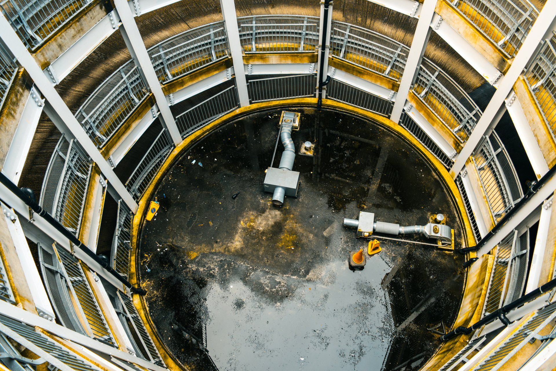 Looking down inside a cylindrical structure with metal walkways and pipes; dark floor.