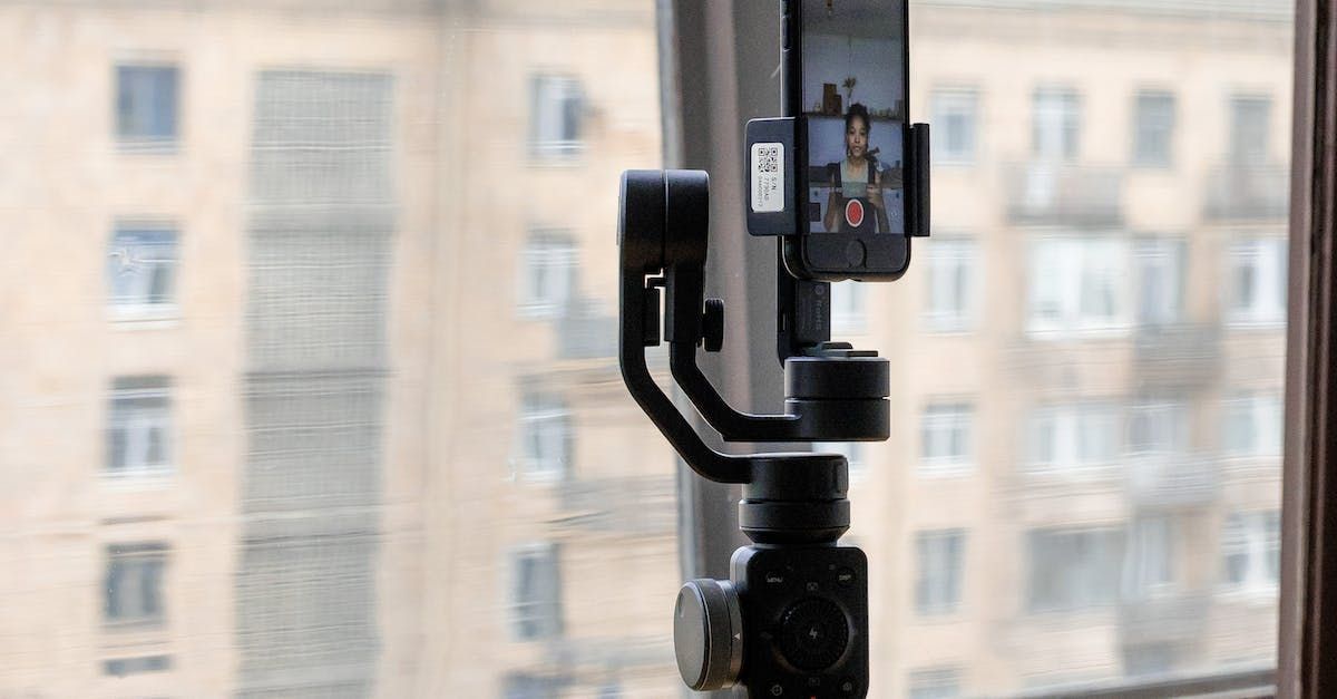 A cell phone is sitting on a tripod in front of a window.